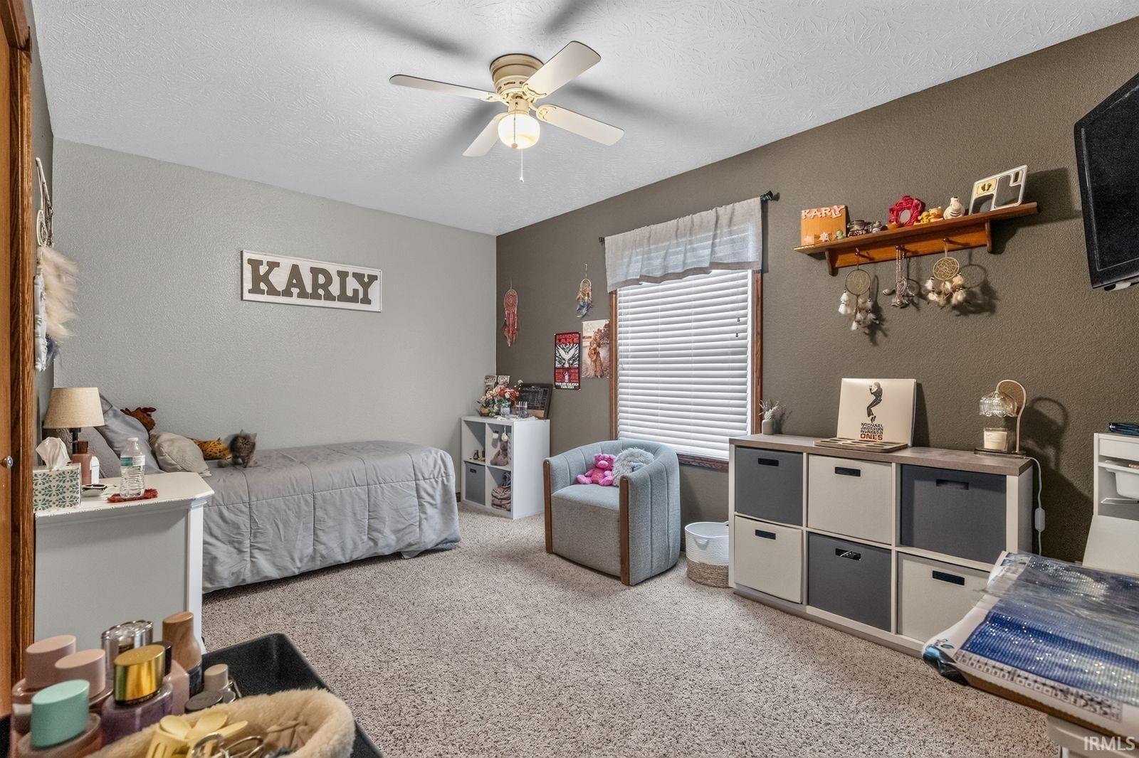 Carpeted room featuring a ceiling fan with light fixture, window with blinds, and built-in shelving