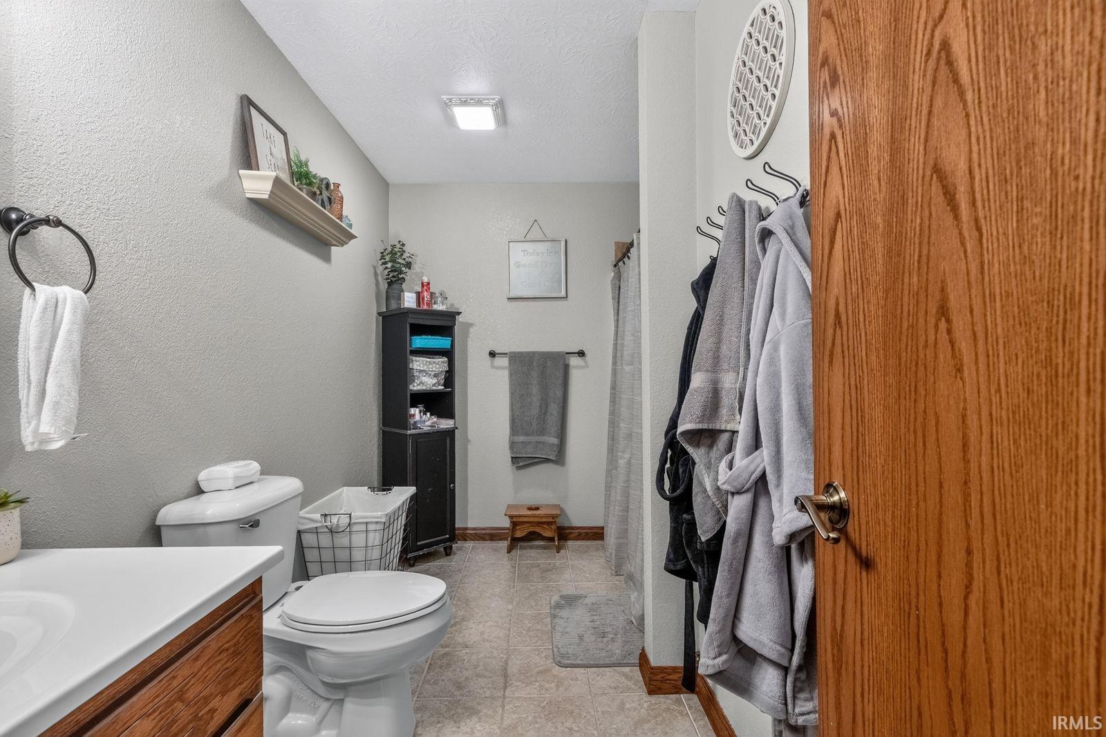 Bathroom featuring a wood-finish vanity with a white countertop, tile flooring, a built-in shelving unit, and a square ceiling light fixture