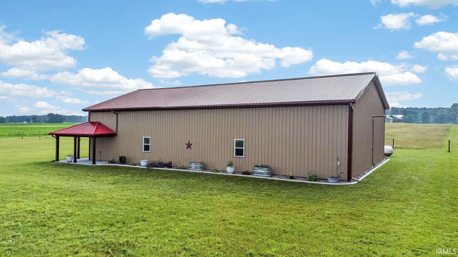 Large pole barn structure featuring tan metal siding and a red metal roof