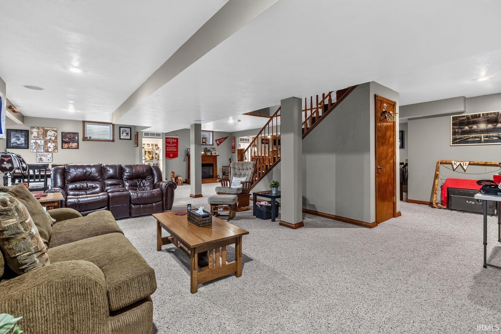 Spacious finished lower level featuring recessed lighting, light-toned carpet, a built-in fireplace with mantel, and a wooden staircase