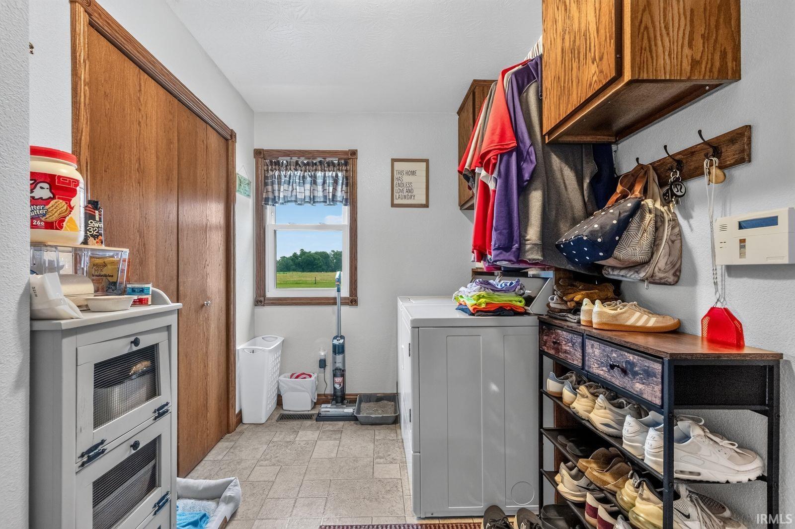 Dedicated laundry area featuring a window with exterior scenery, wood-finish cabinetry, and tiled flooring
