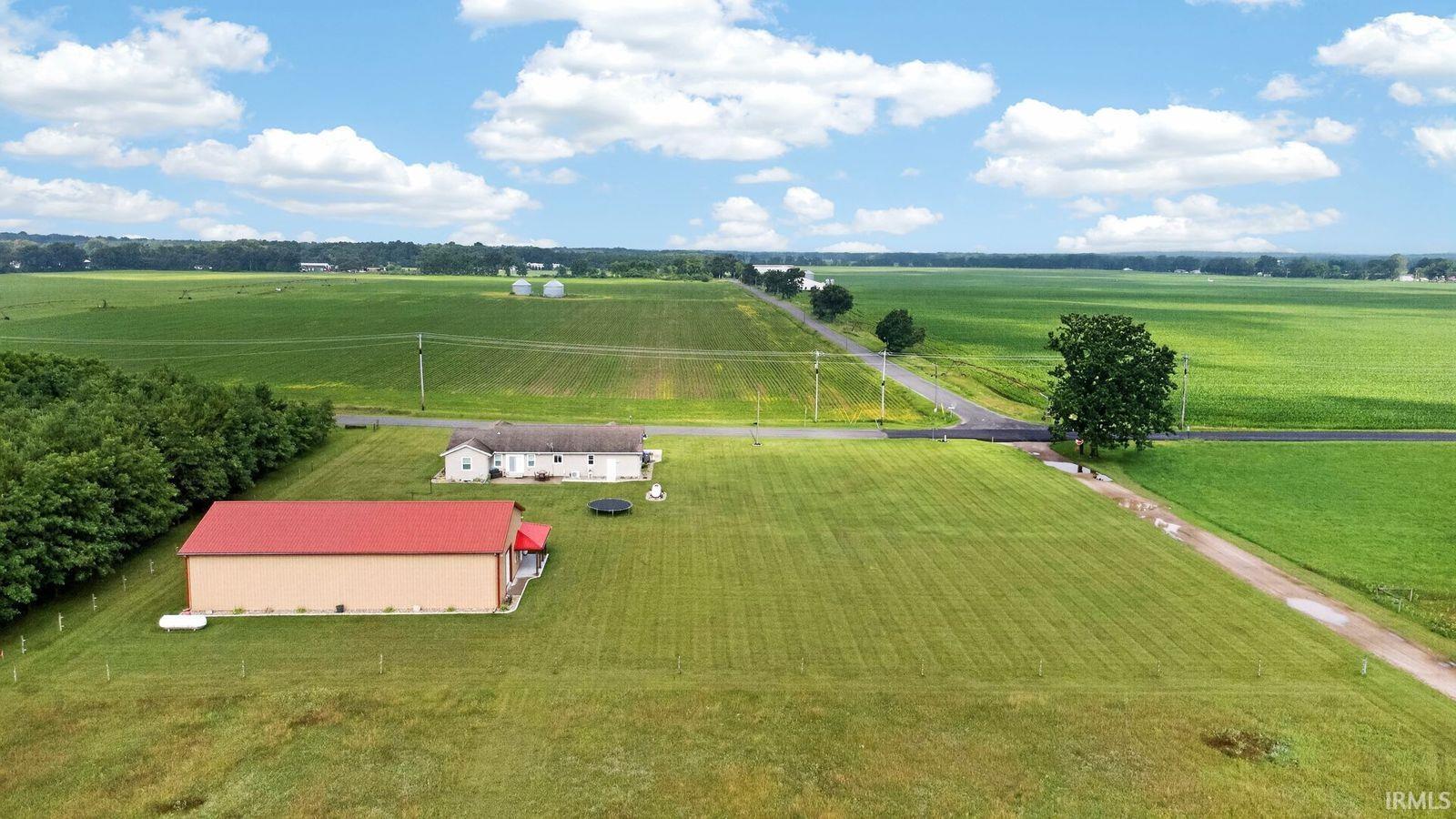 Expansive rural property featuring a primary residence with light-colored siding and a substantial outbuilding with a red metal roof