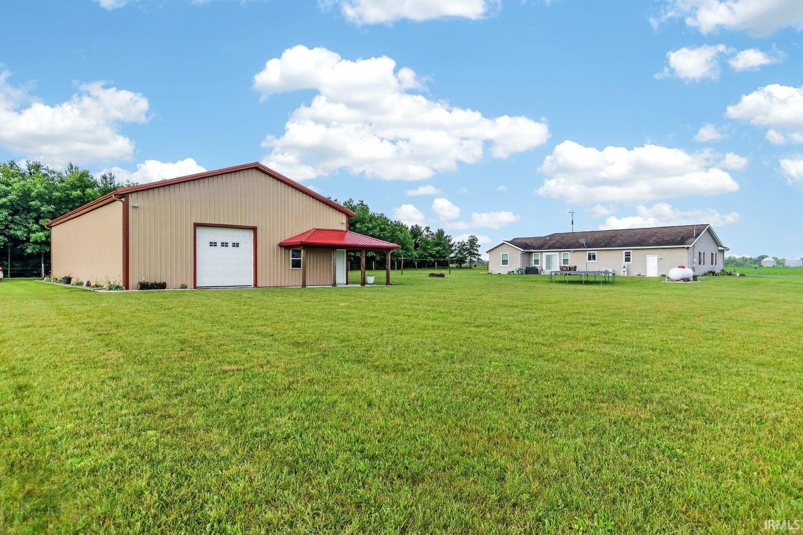 Metal-sided outbuilding featuring a red pitched roof, a large roll-up garage door, and a covered porch entry