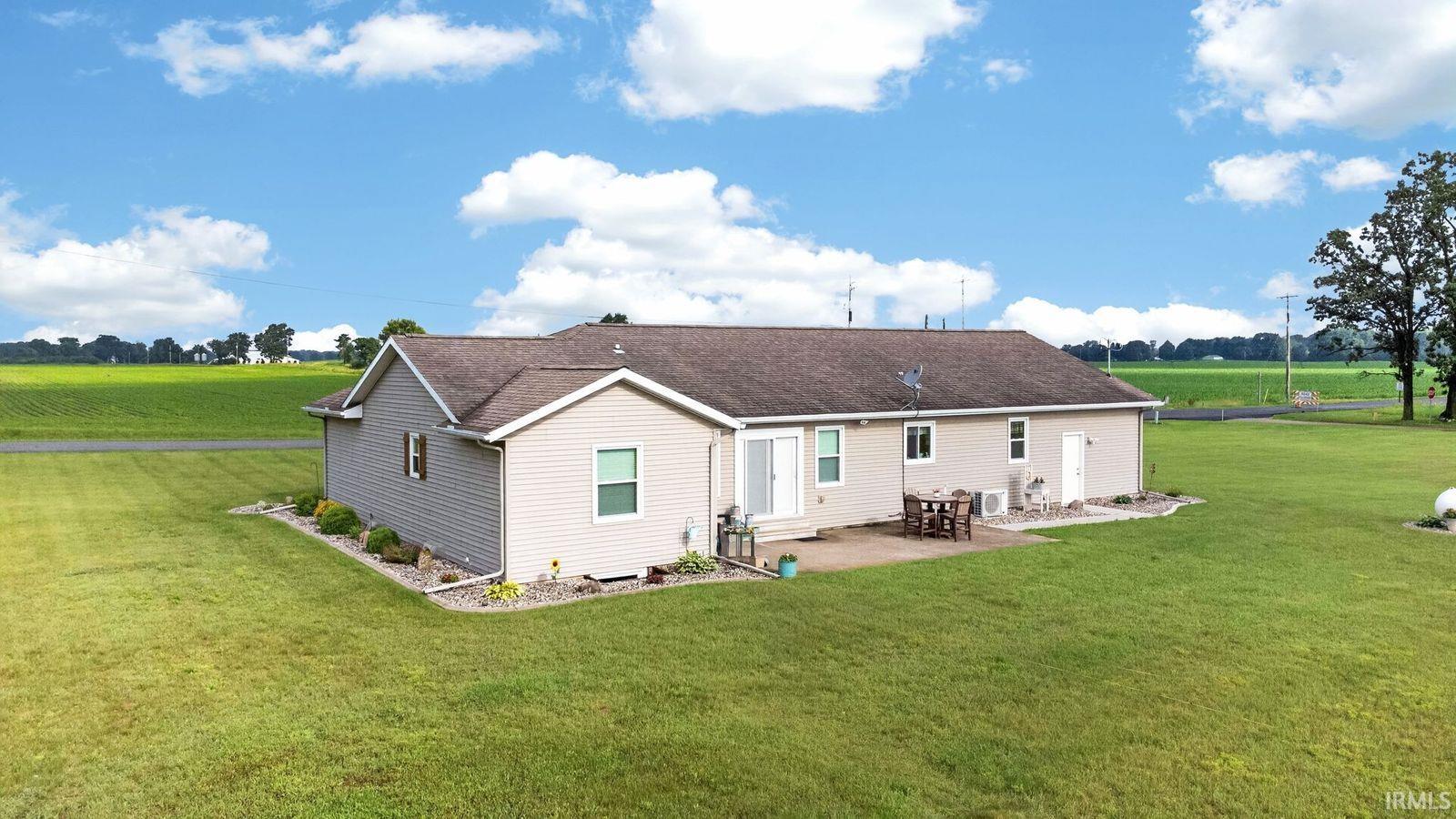 Ranch-style residence featuring light-colored siding, a brown shingle roof, and a concrete patio