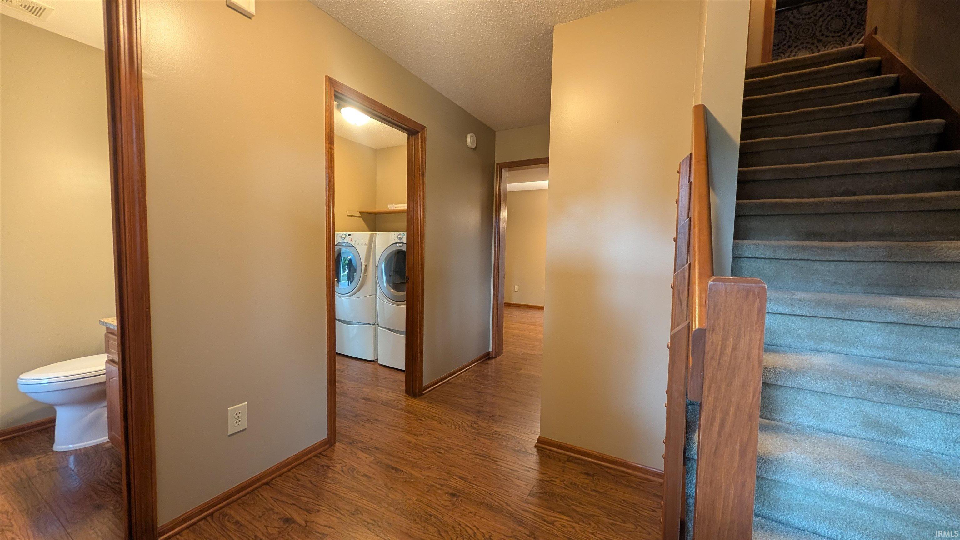 Wood-finish flooring throughout the hallway, leading to a utility room with built-in shelving, and a separate half-bath with a toilet and vanity