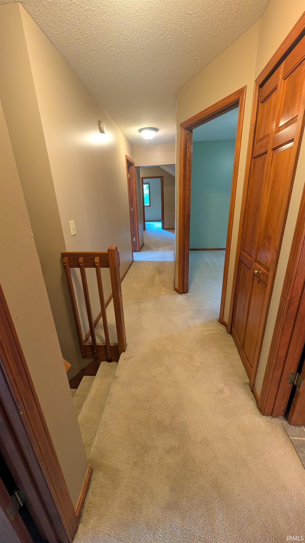 Carpeted hallway with wood trim and doors, featuring recessed lighting and a staircase with a wood railing
