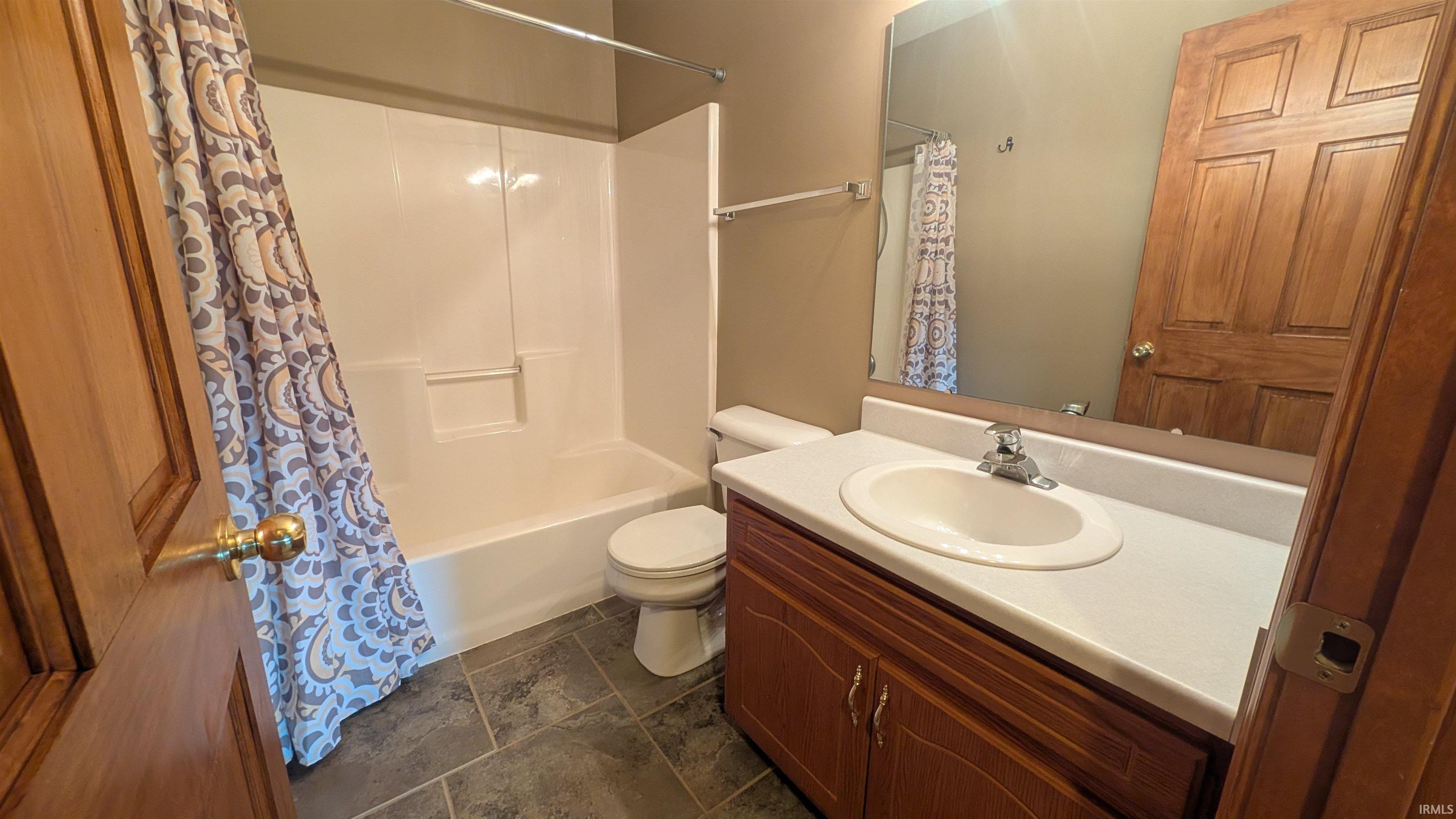 Bathroom featuring a white tub and shower combination, a toilet, a vanity with a white countertop and integrated sink, and wood-finish cabinetry