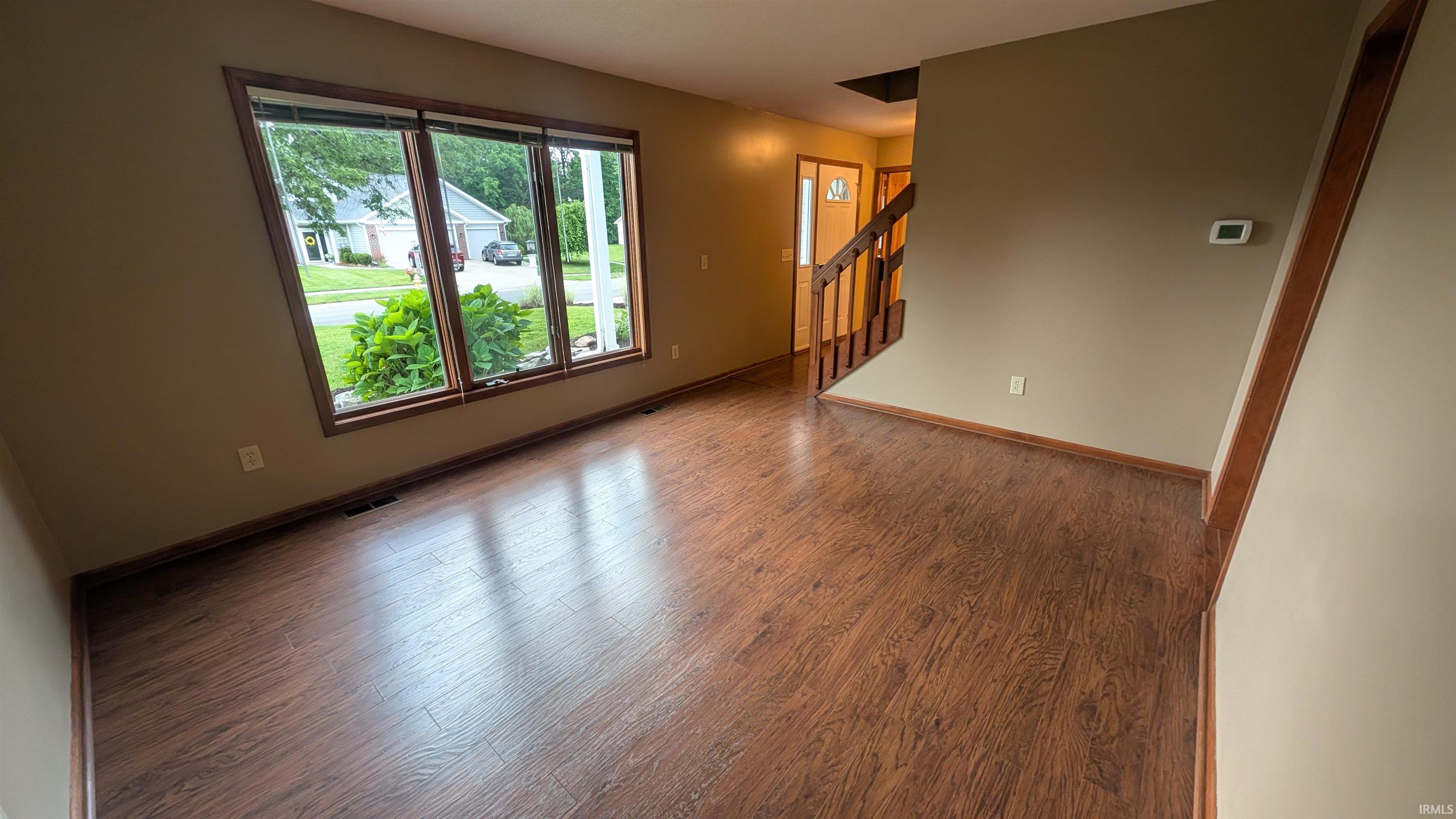 Spacious room featuring wood-finish flooring, a large bay window with wood trim, and neutral wall tones