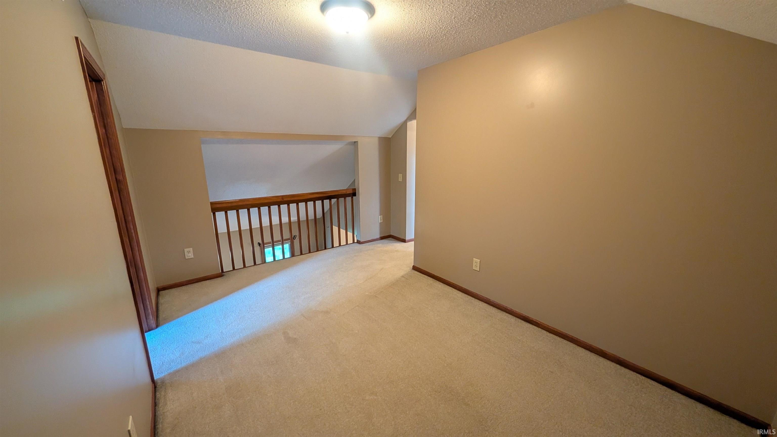 Carpeted loft area featuring a wood railing overlooking a lower level, neutral wall paint, a built-in light fixture, and a wood trim baseboard