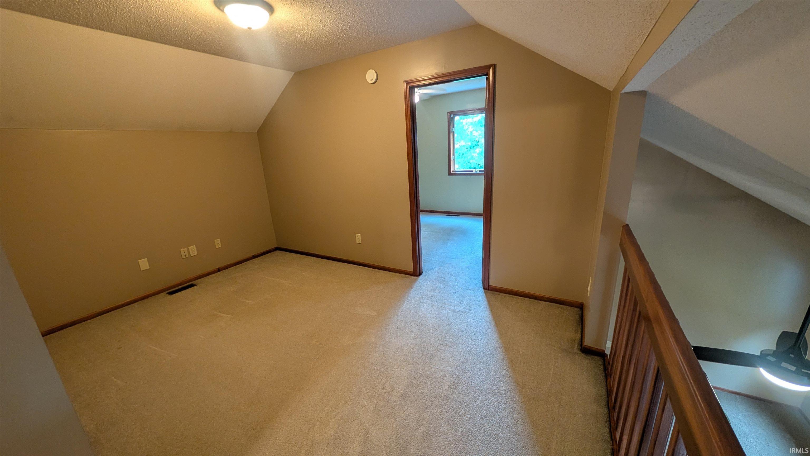 Carpeted room featuring a ceiling-mounted light fixture, sloped ceilings, and baseboard trim
