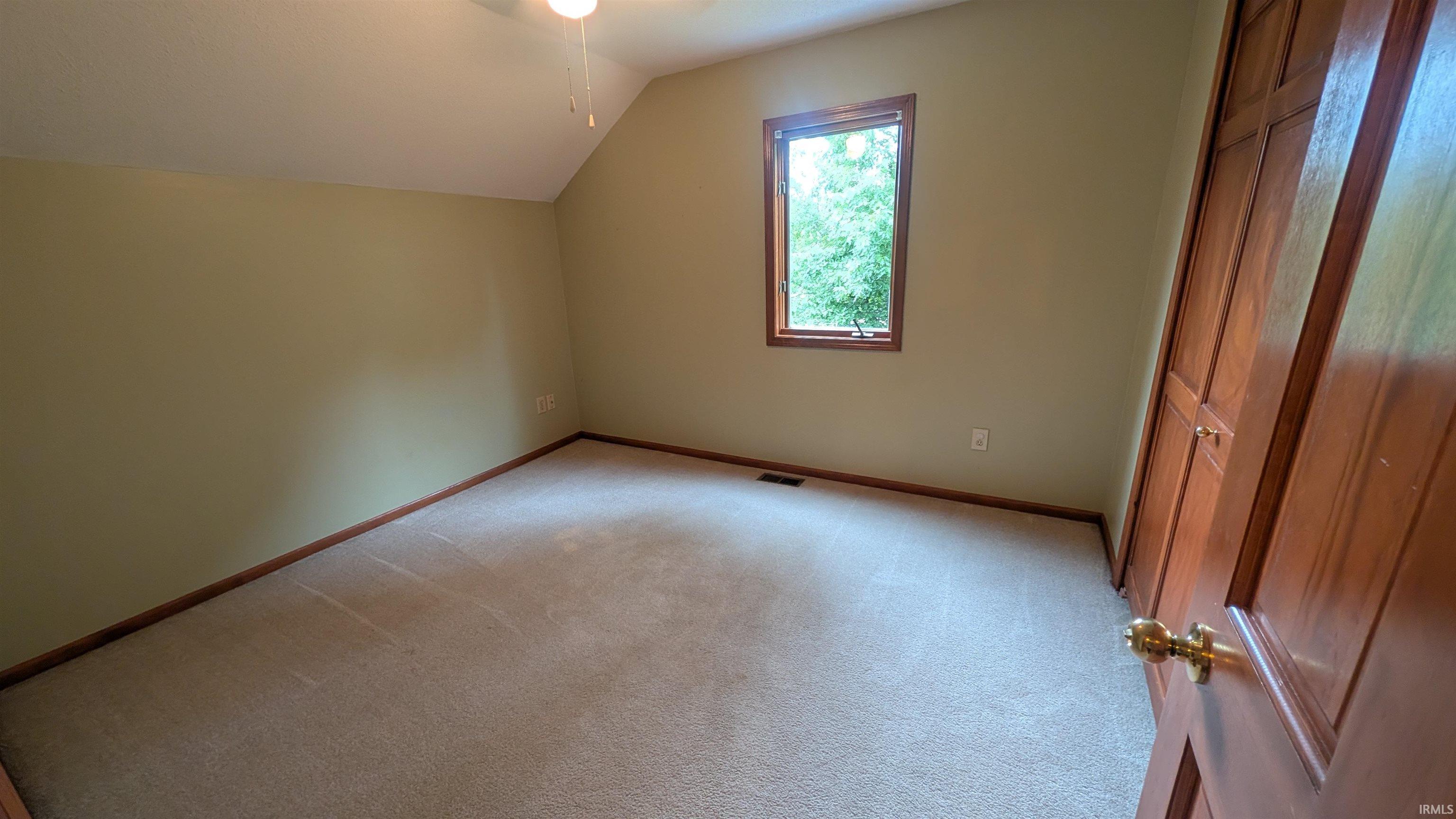 Carpeted room featuring a single window with wood trim, neutral wall color, and a wood bi-fold closet
