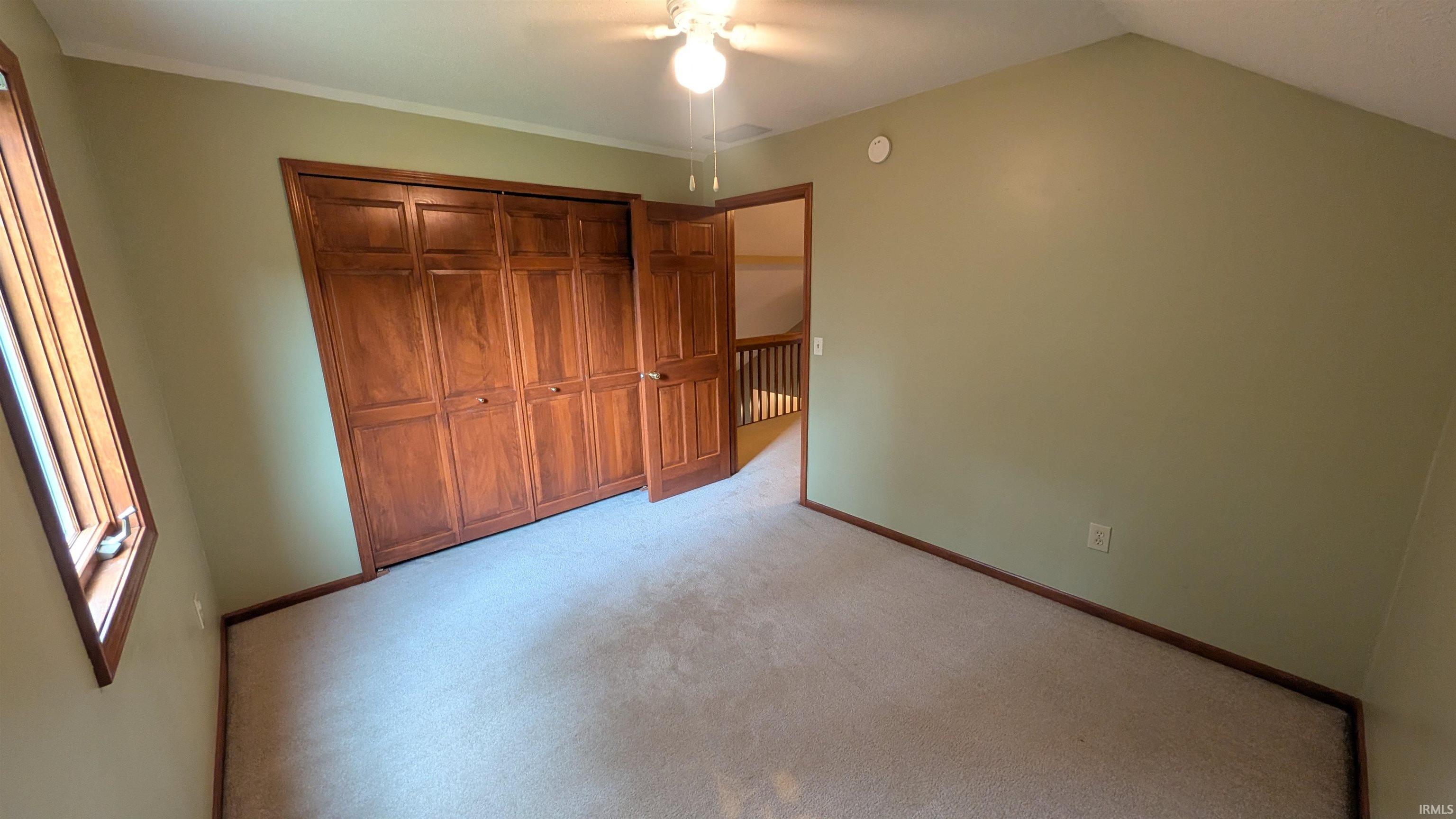 Carpeted room featuring a ceiling fan, a window with wood trim, wood-finish bi-fold closet doors, and wood-finish trim