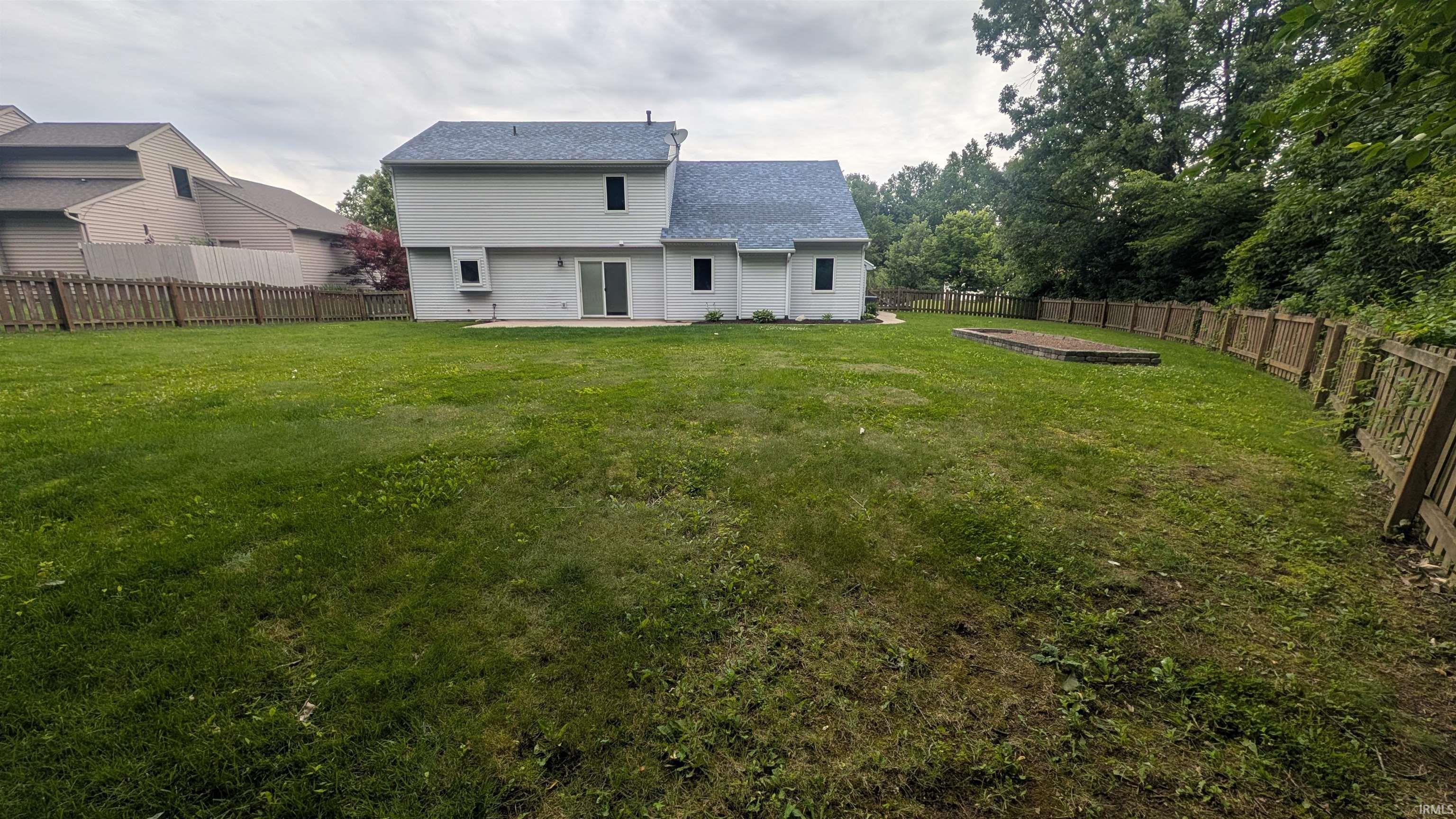 Expansive green lawn featuring a wooden privacy fence, a raised garden bed, and mature perimeter trees