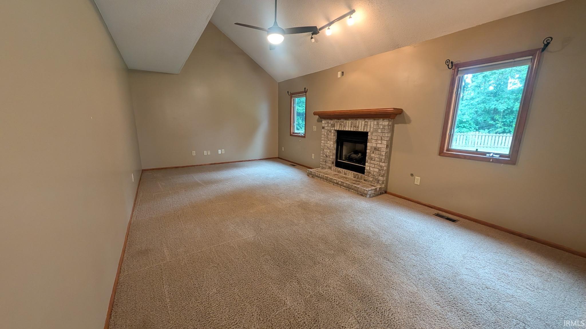Vaulted ceiling living space featuring a brick fireplace with a wood mantle, carpet flooring, and multiple windows
