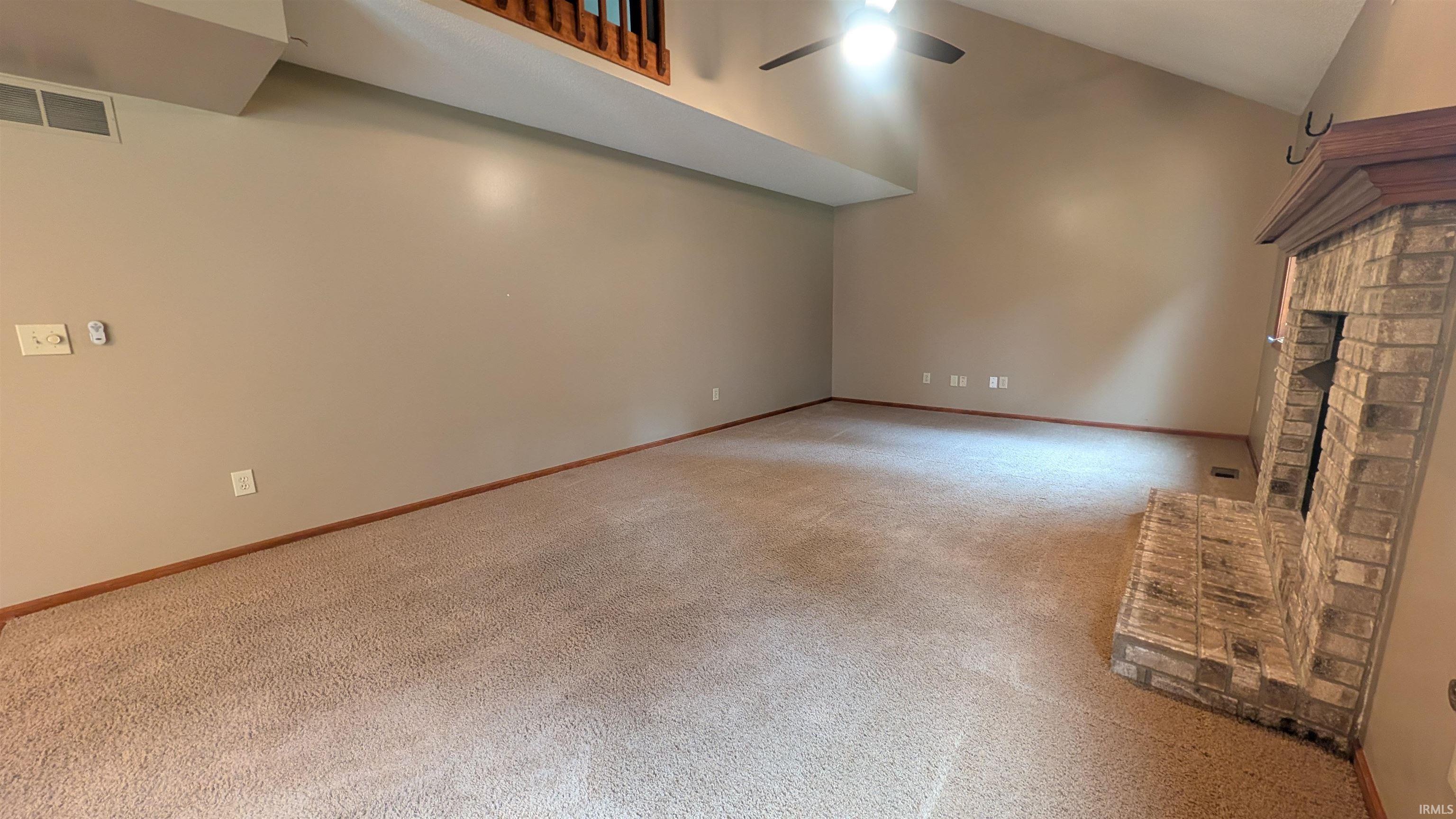 Spacious room featuring vaulted ceilings, a ceiling fan with integrated lighting, and a brick fireplace with a wood mantle