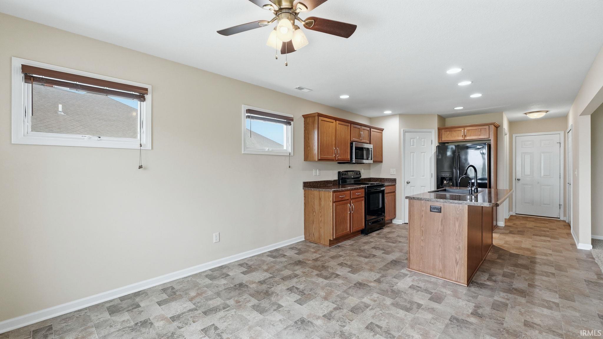 Kitchen area featuring wood-finish cabinetry, black appliances, and a central island with a sink