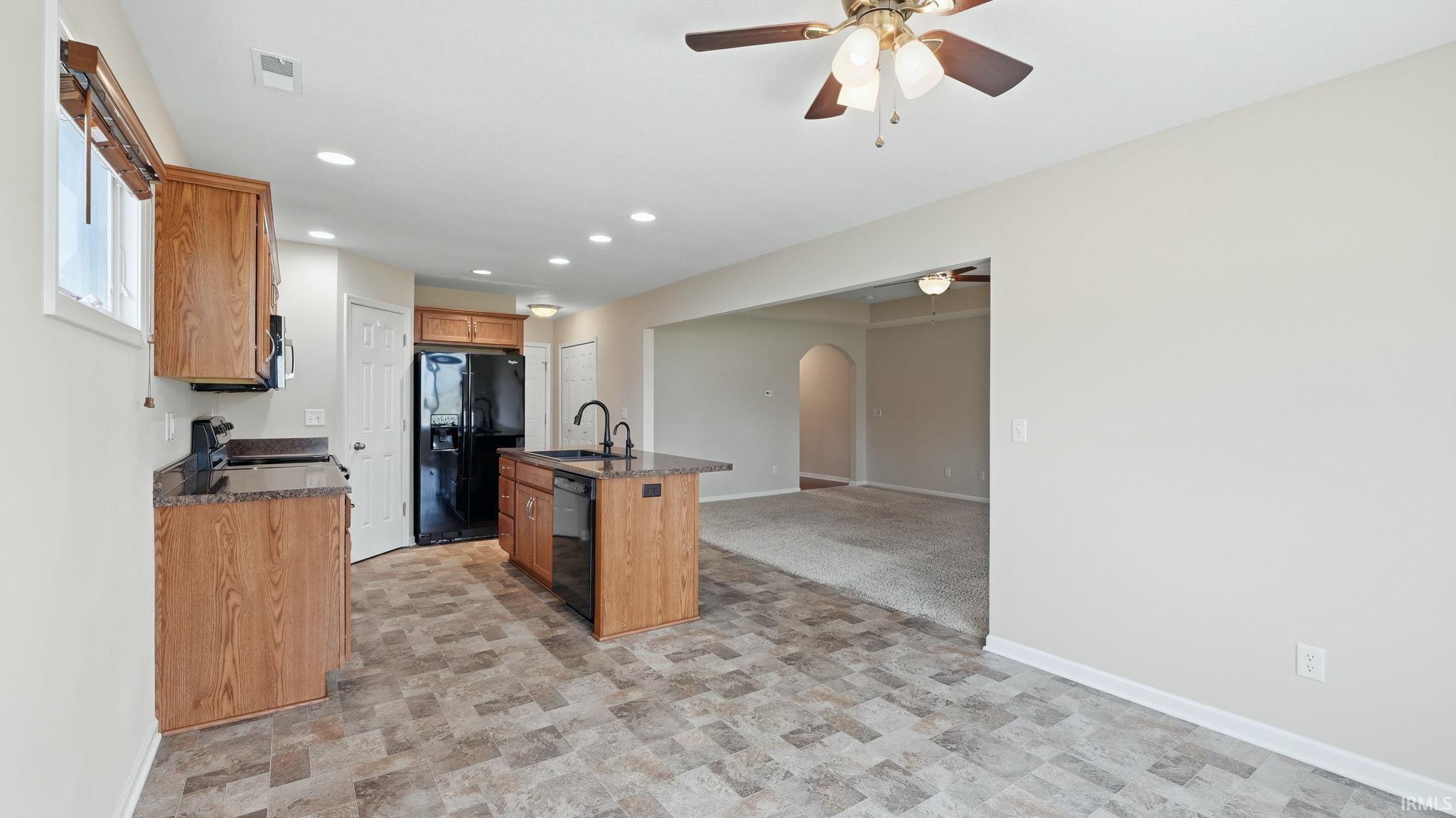 Kitchen featuring wood cabinetry, dark countertops, black appliances, and an island with a sink
