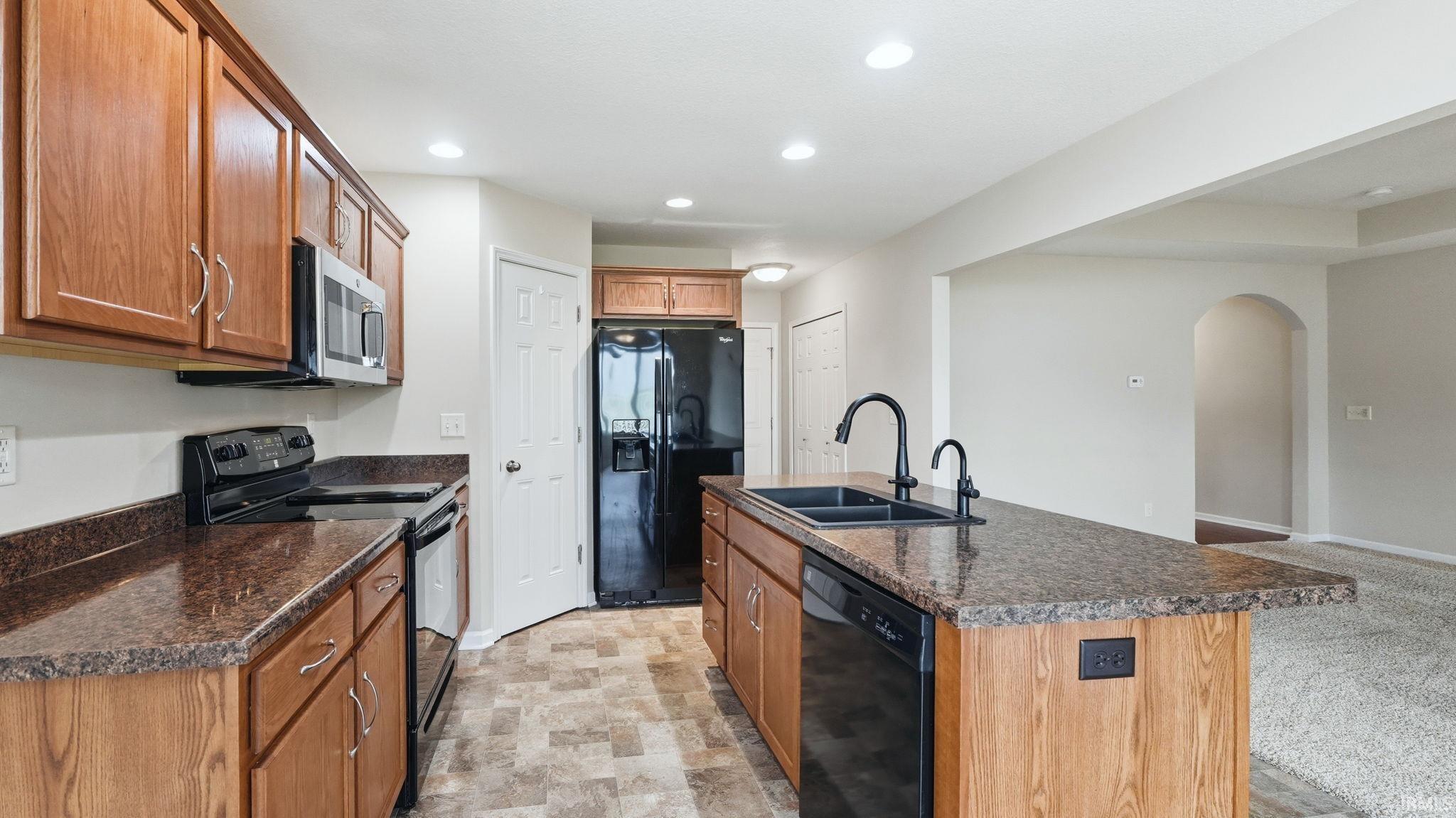 Kitchen featuring wood cabinetry, dark-toned countertops, and a central island with a double sink and black faucet