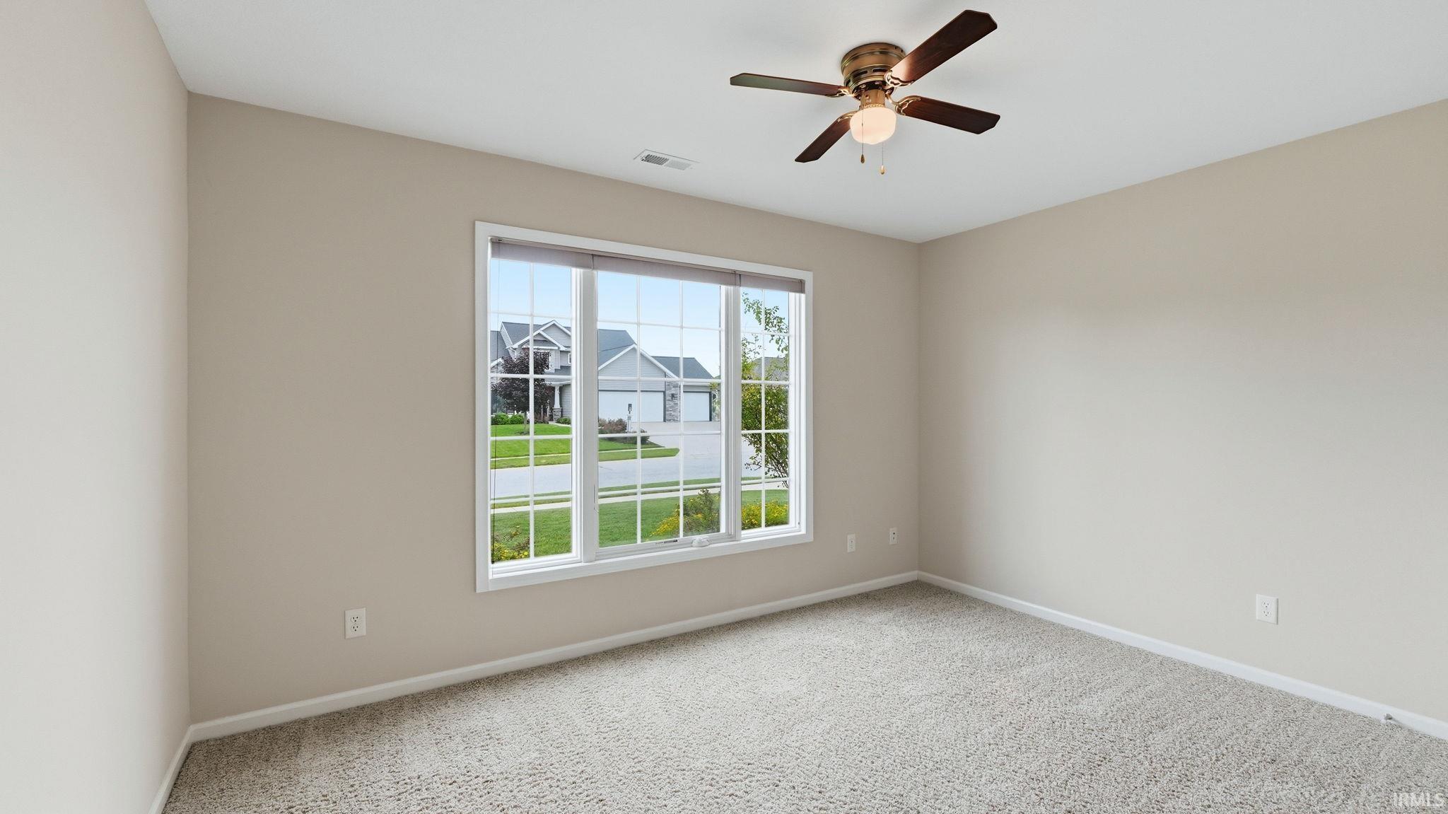 Carpeted room with a multi-pane window, neutral-toned walls, and a ceiling fan with integrated lighting