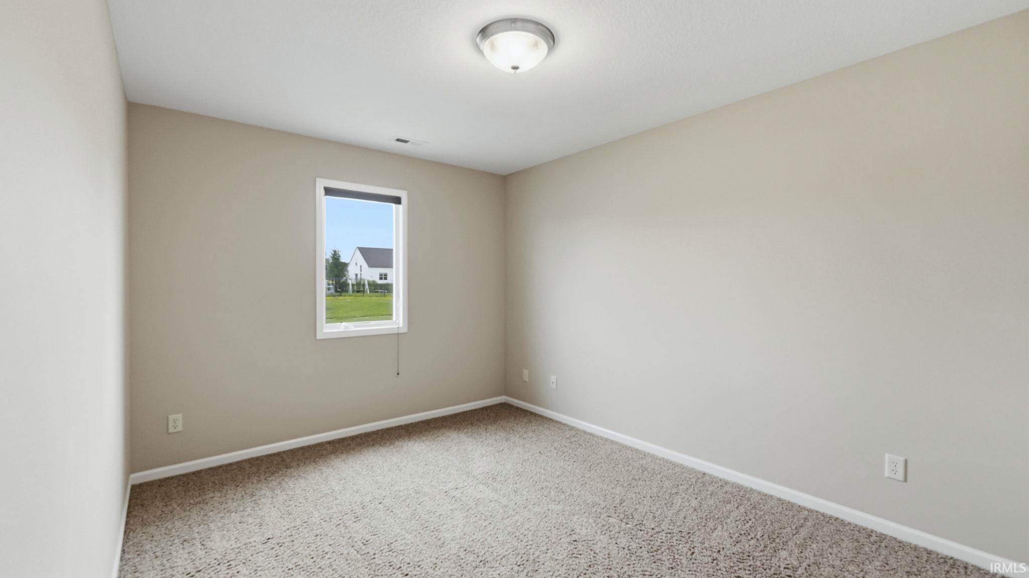 Neutral-toned room featuring a single window with white trim, tan carpeting, and a flush-mount ceiling light fixture