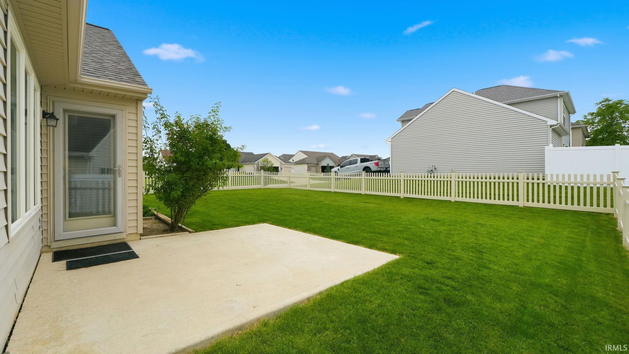 Expansive green lawn featuring a concrete patio, white picket fencing, and a full-view storm door