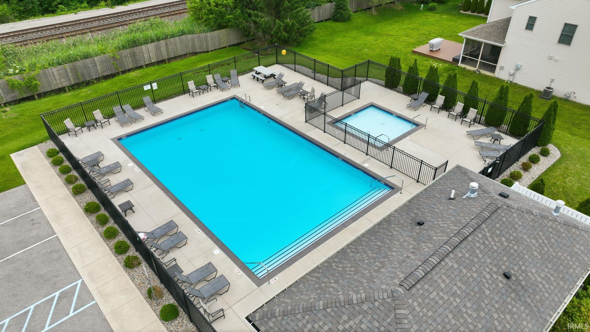 Expansive outdoor amenity area featuring a rectangular swimming pool with integrated steps, a separate square spa, and surrounding concrete decking