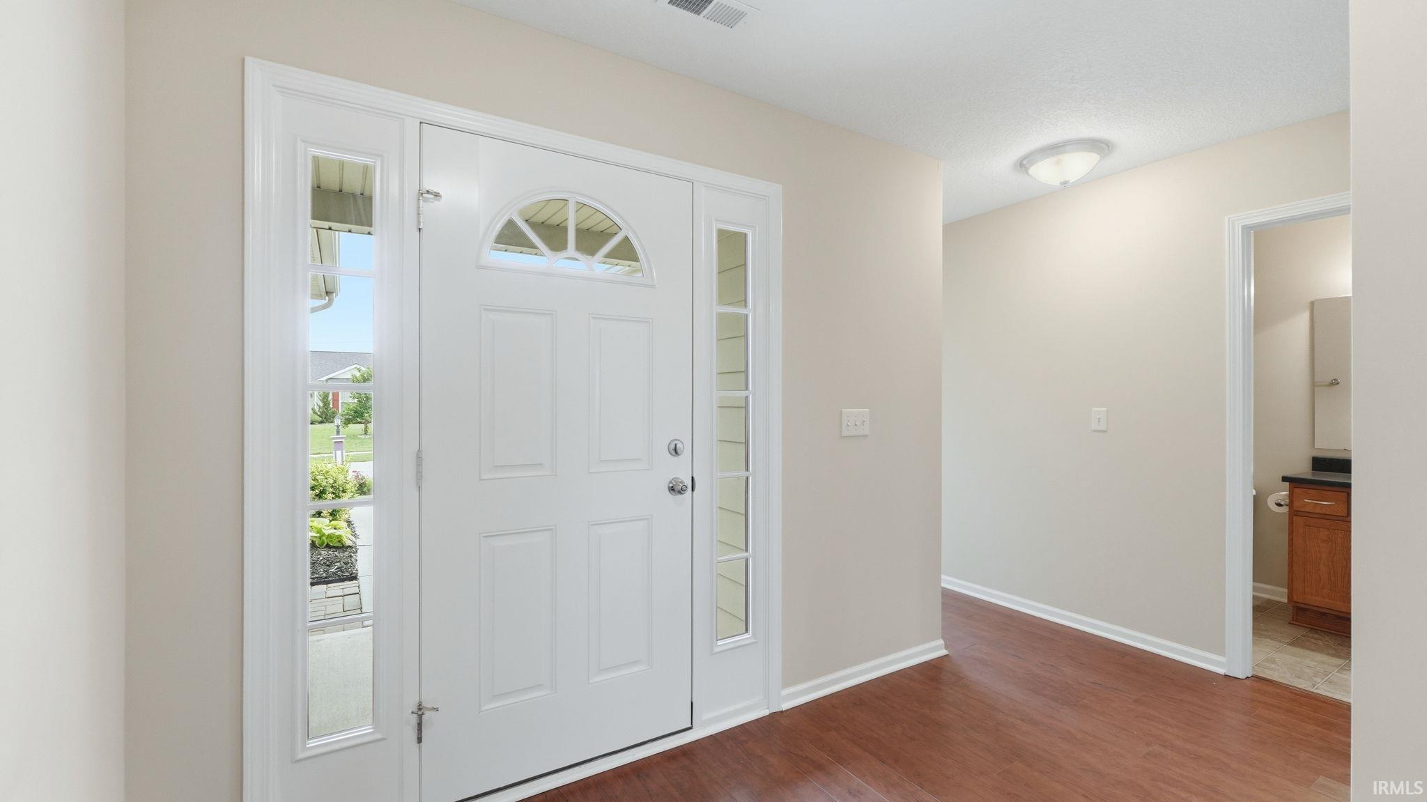 Entryway featuring a paneled door with an arched transom window, flanking sidelights, wood-finish flooring, and neutral wall tones