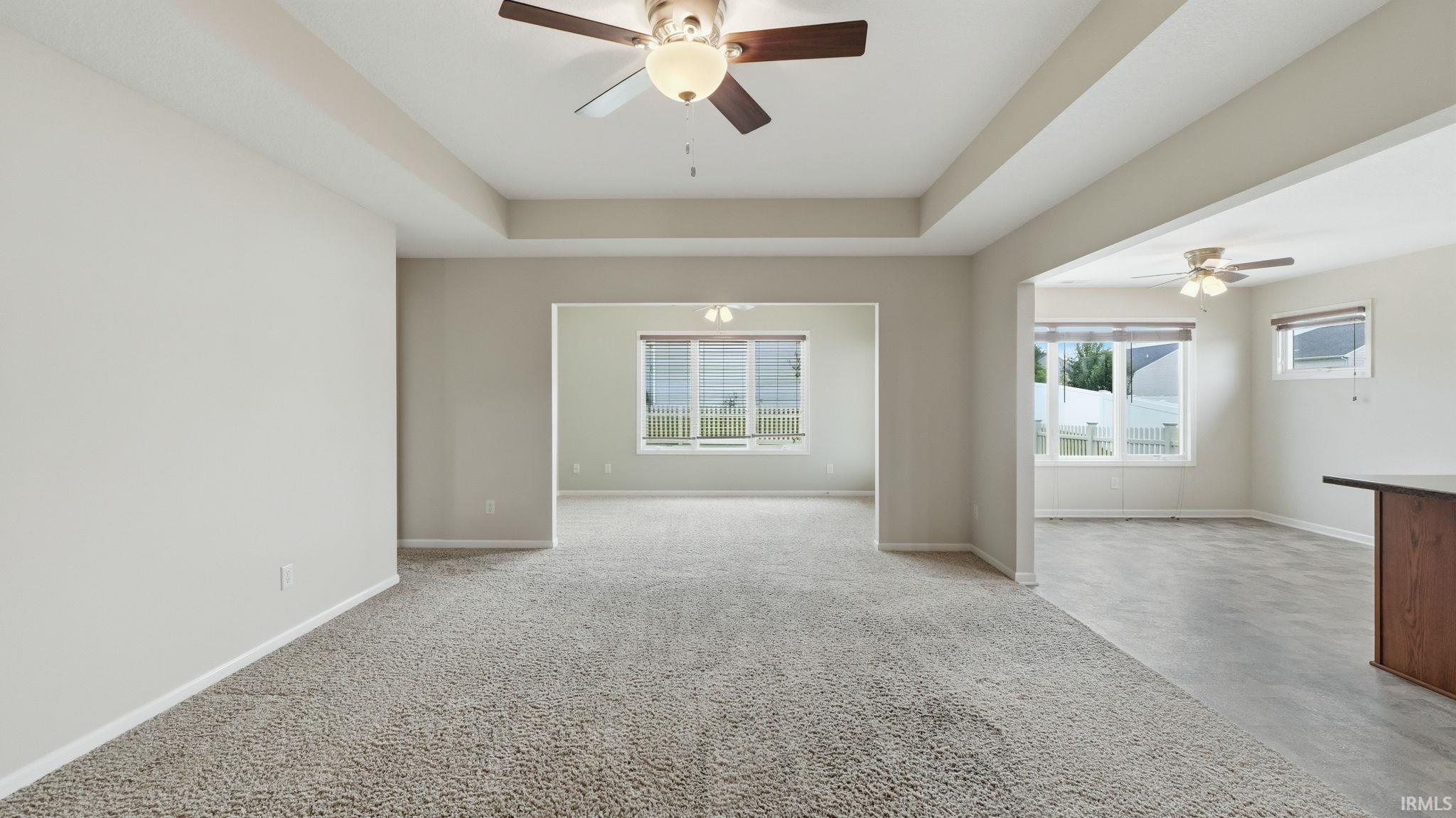 Spacious room featuring tray ceiling, ceiling fan with light fixture, neutral carpeting, and arched entryway