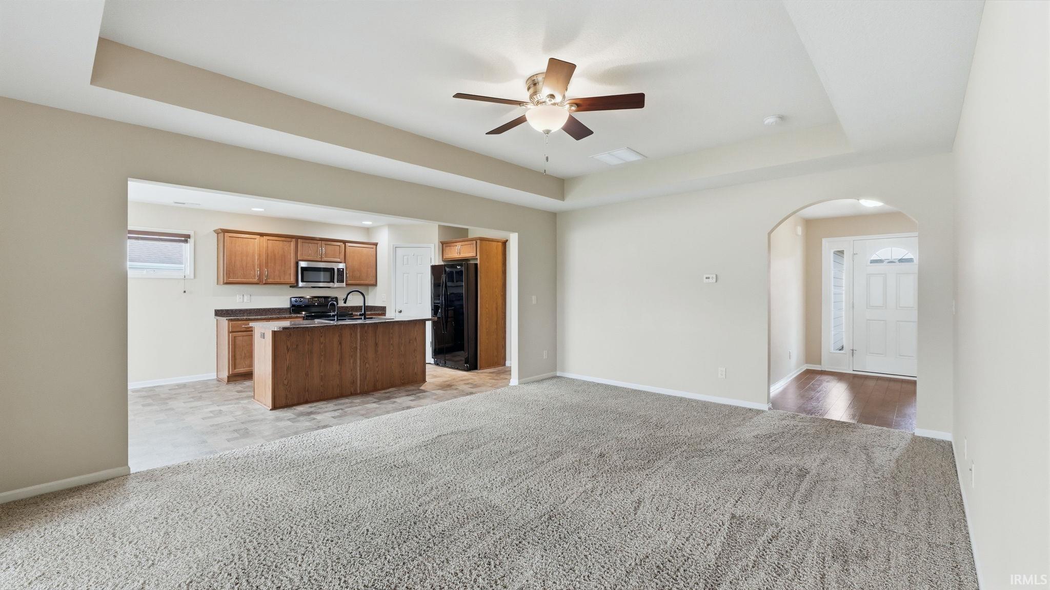 Spacious living area featuring light-toned carpeting and tray ceiling with a ceiling fan