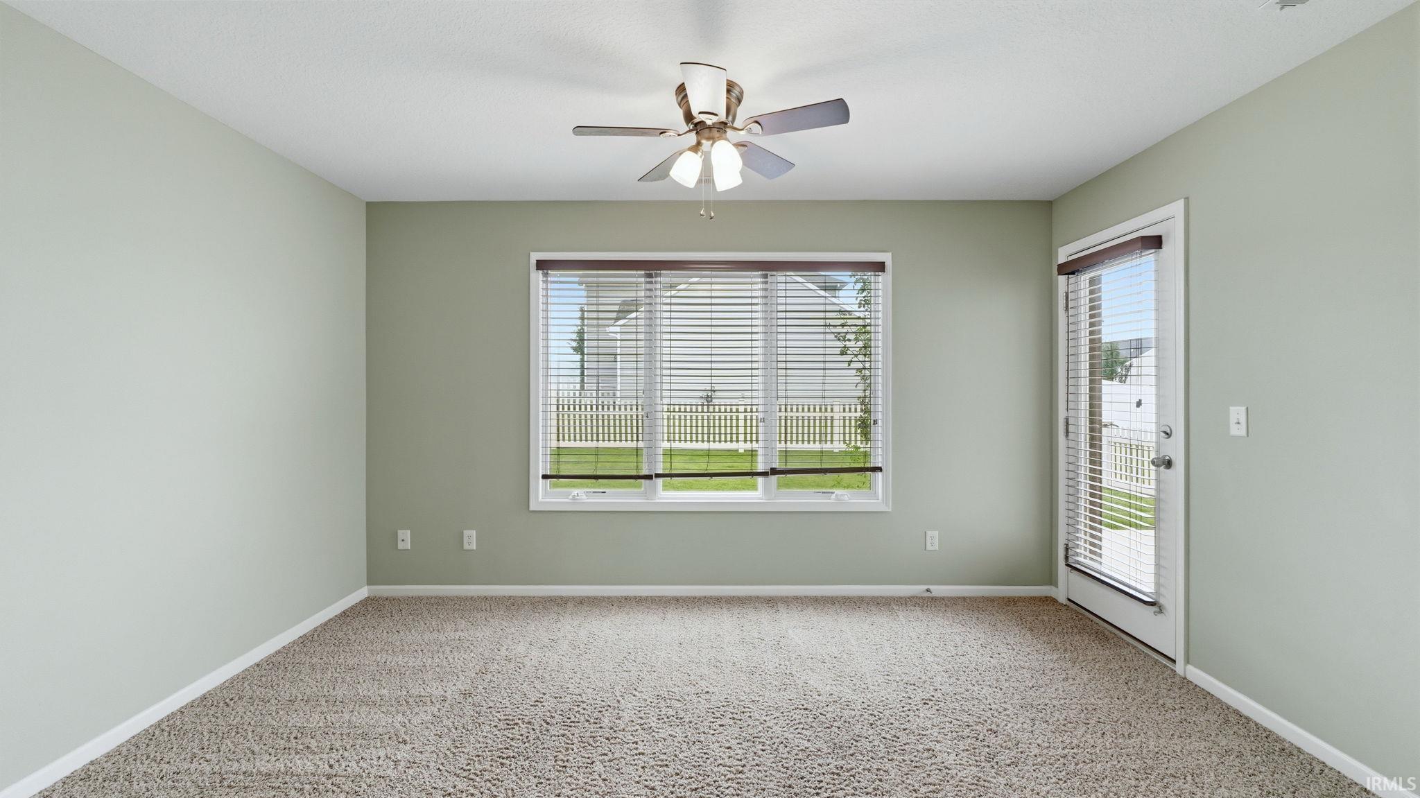 Carpeted room featuring a ceiling fan with integrated lighting, a large window with blinds, and a glass-paneled door