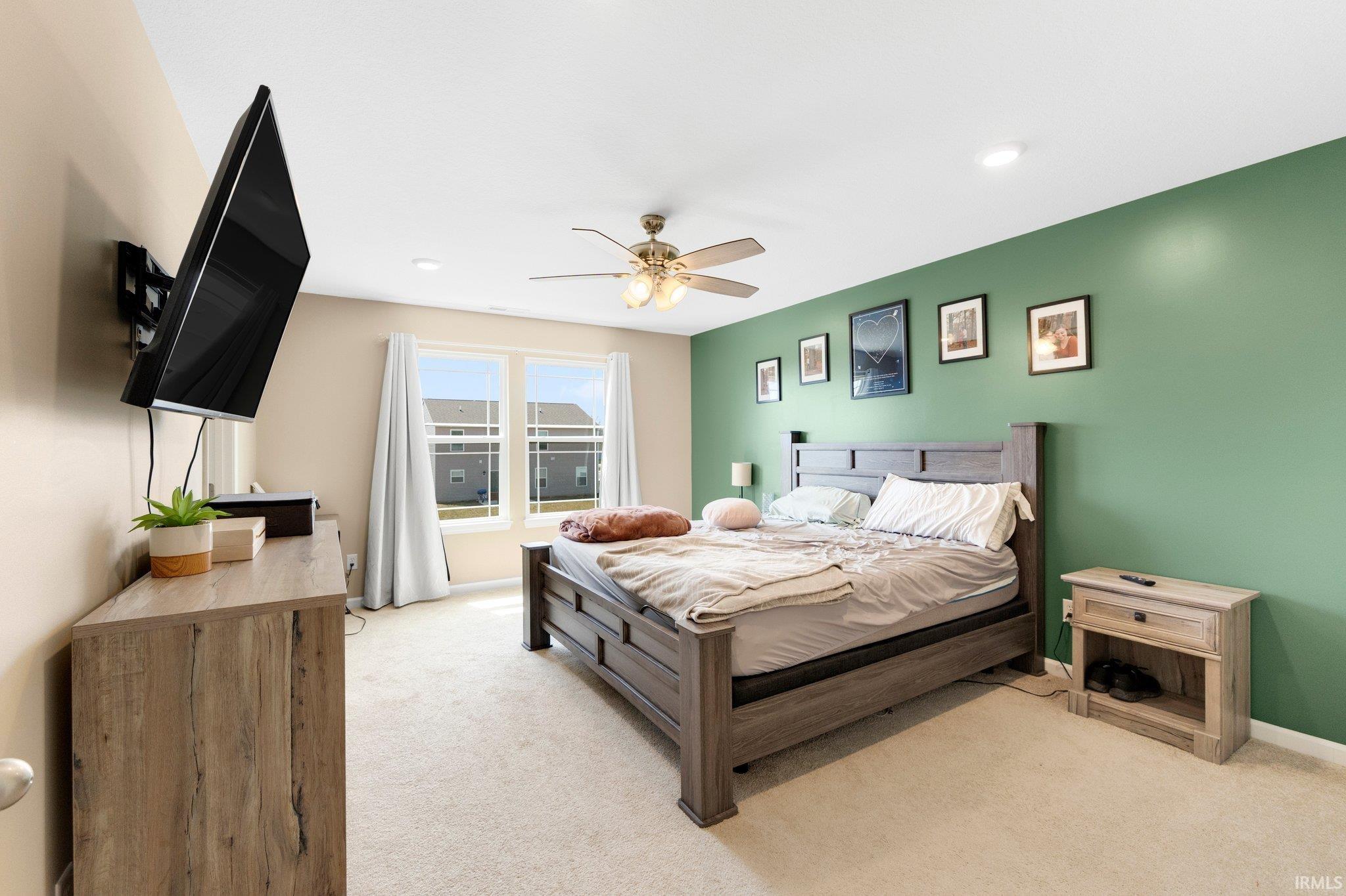 Spacious bedroom featuring light neutral carpeting, dual windows with white drapery, and a contrasting accent wall