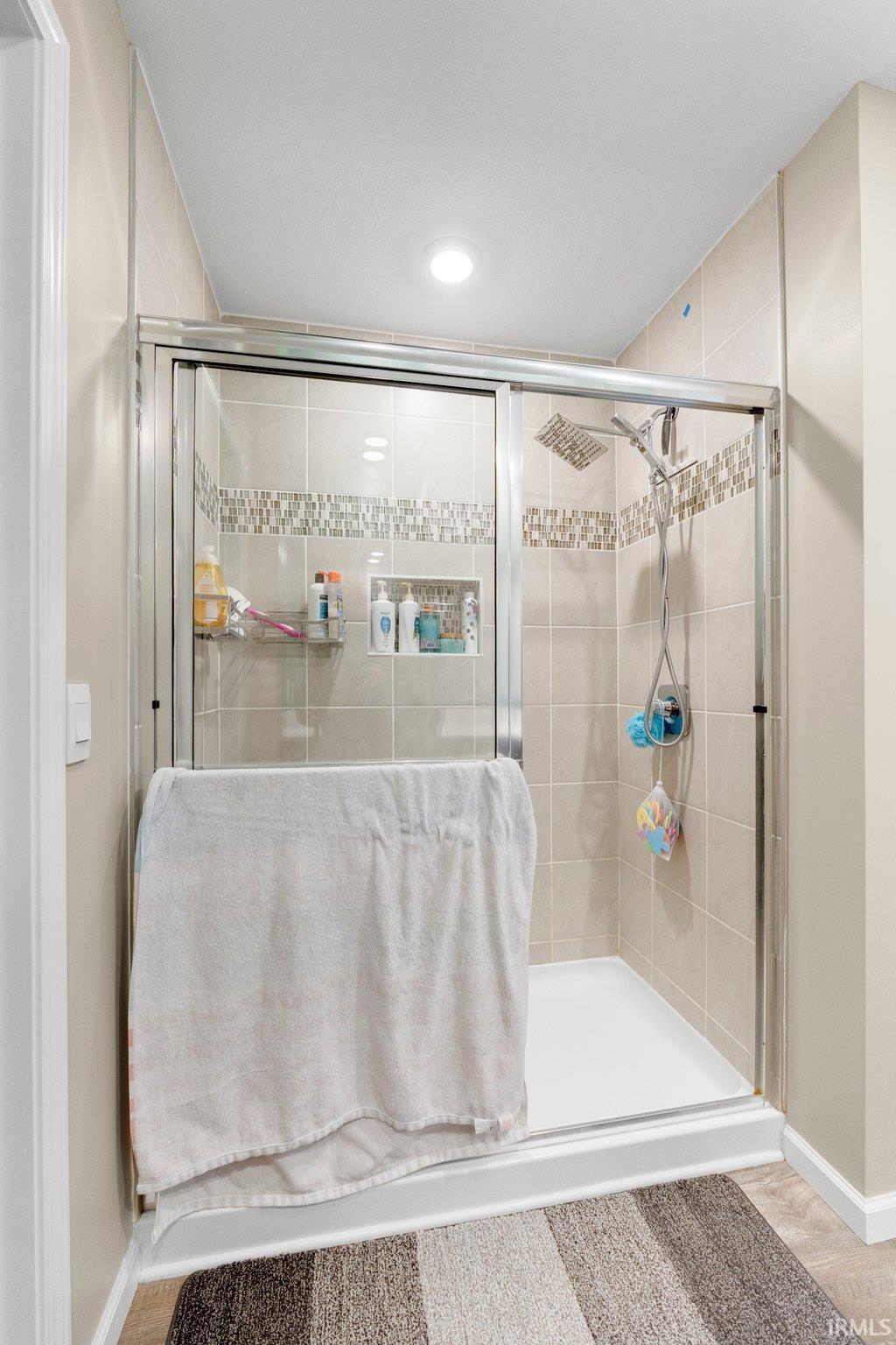 Enclosed shower with sliding glass doors, neutral-toned wall tiles, decorative accent tile band, built-in shower niche, and a rain showerhead