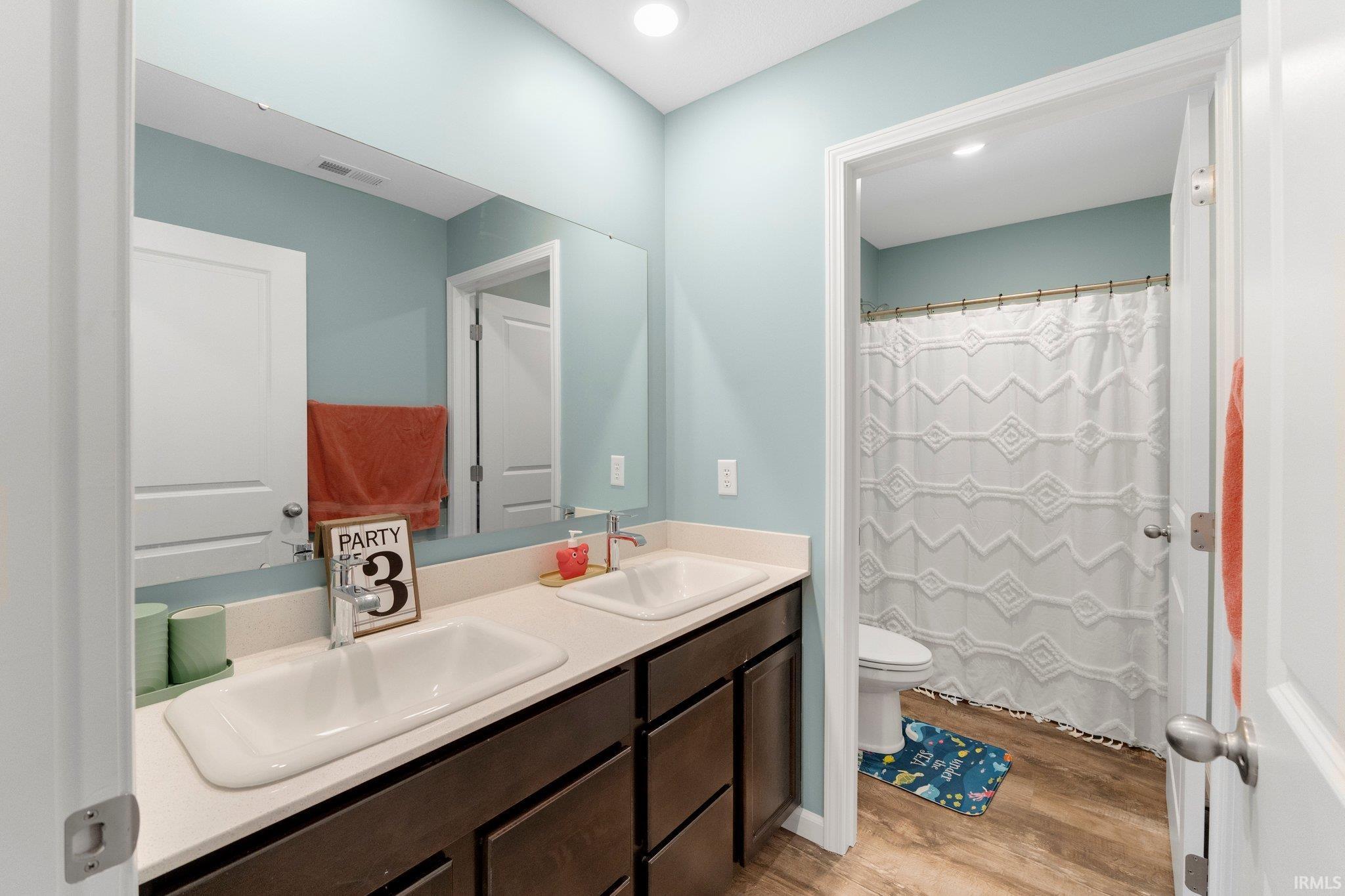 Bathroom featuring a dual vanity with undermount sinks, light-toned countertop, dark wood-finish cabinetry, and a full-width mirror