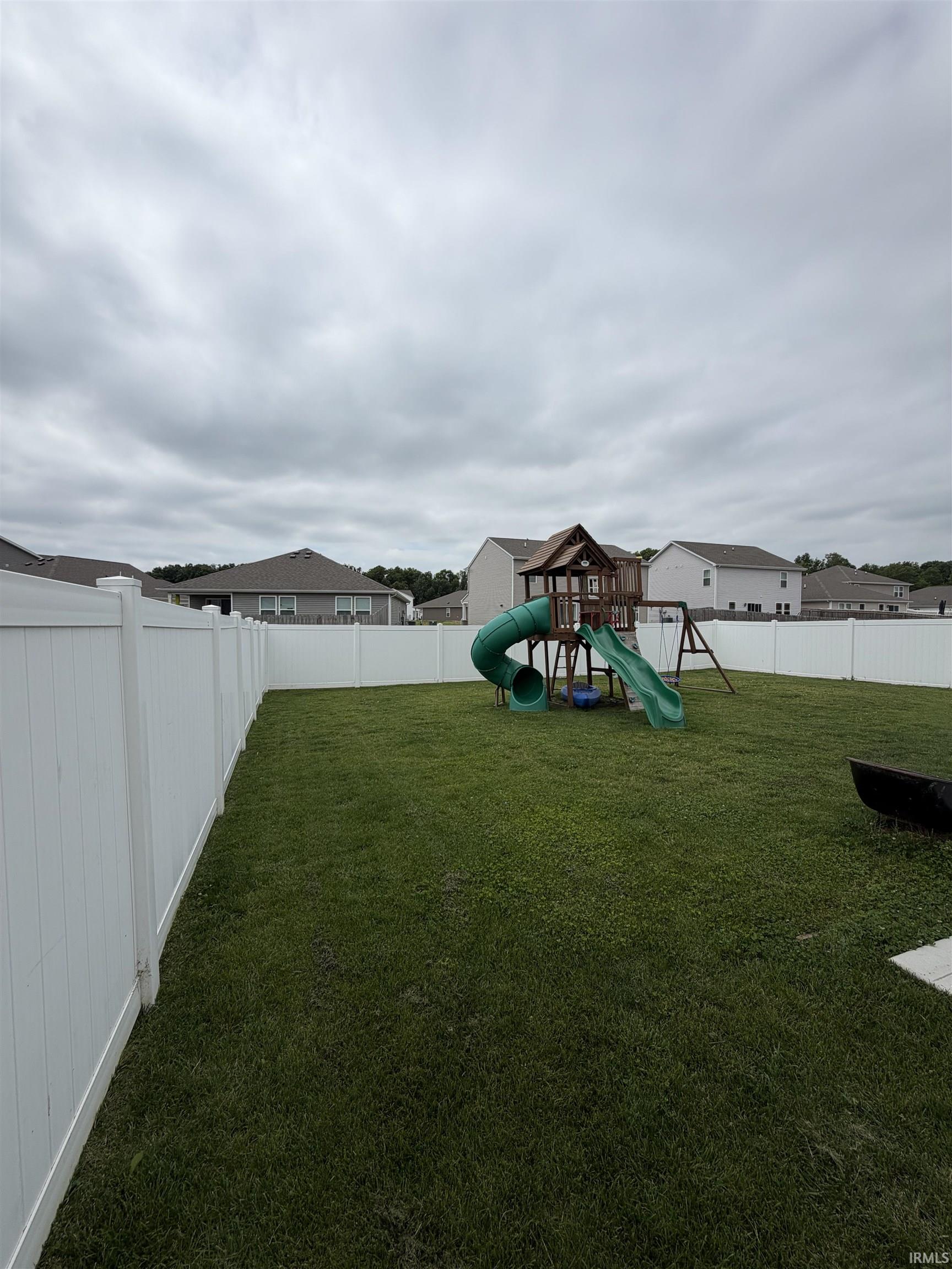Expansive backyard featuring a manicured lawn, a full white vinyl privacy fence, and concrete pavers