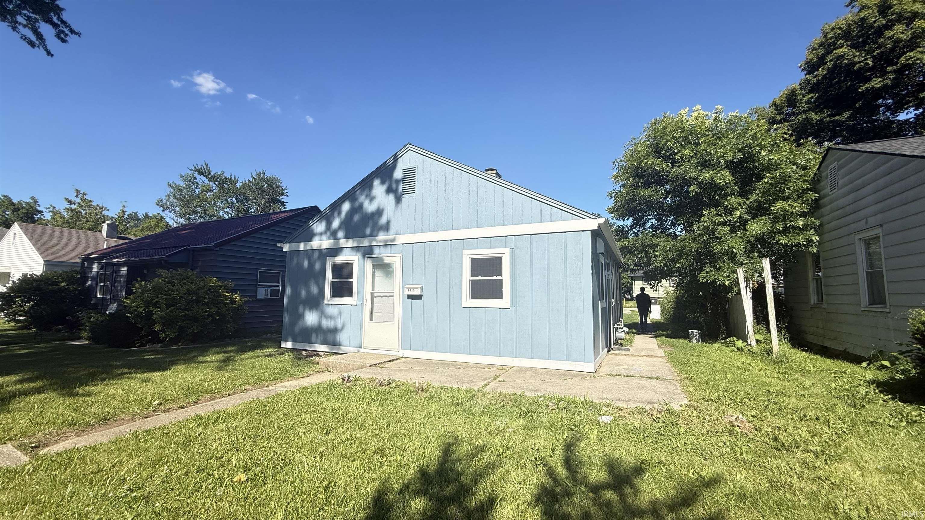 Blue siding exterior with white trim windows and a light-colored entry door