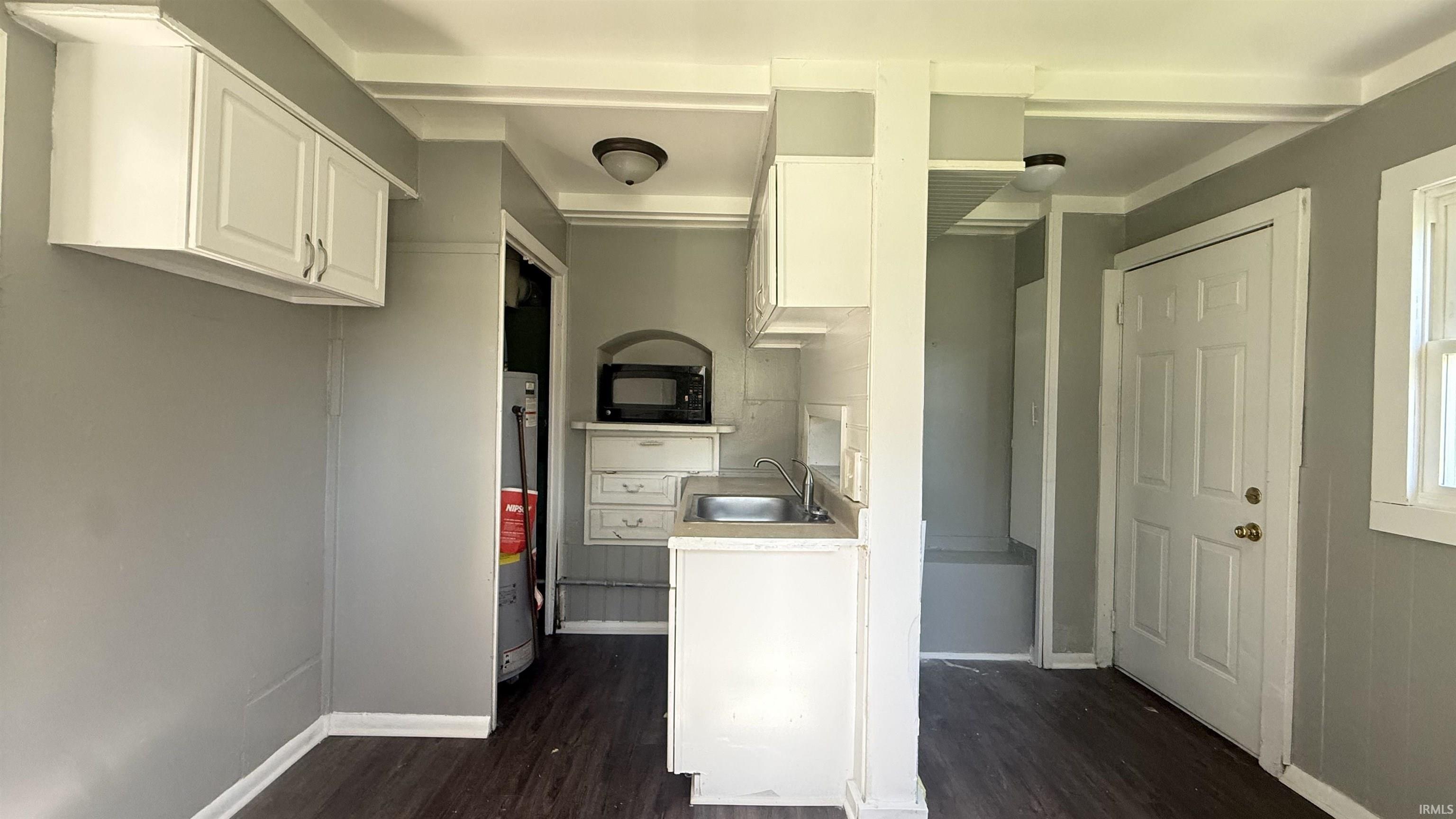Compact kitchen area featuring wood-finish flooring, white cabinetry, and a stainless steel sink