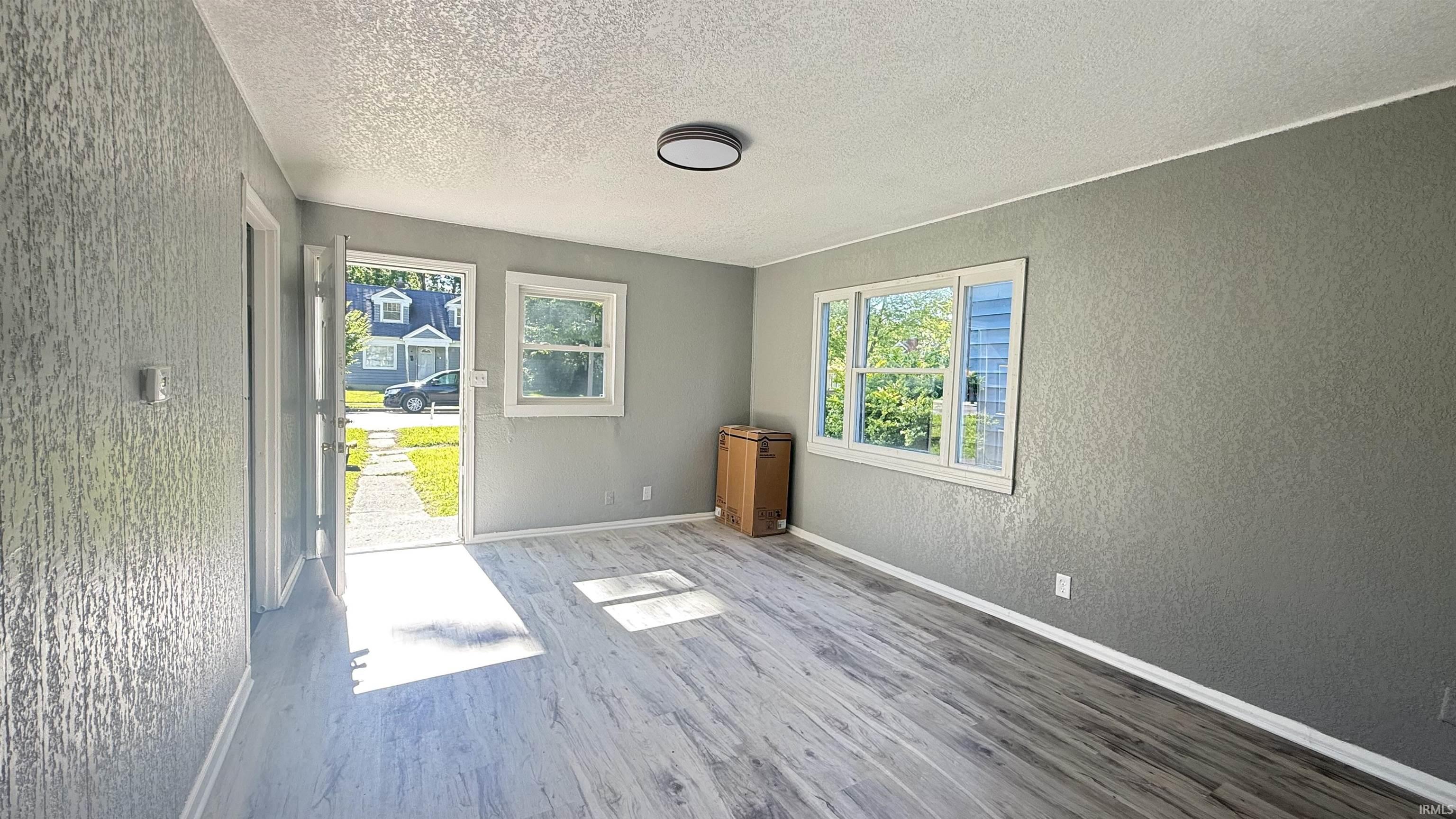 Spacious room featuring wood-finish flooring, two windows, a ceiling-mounted light fixture, and textured wall finishes