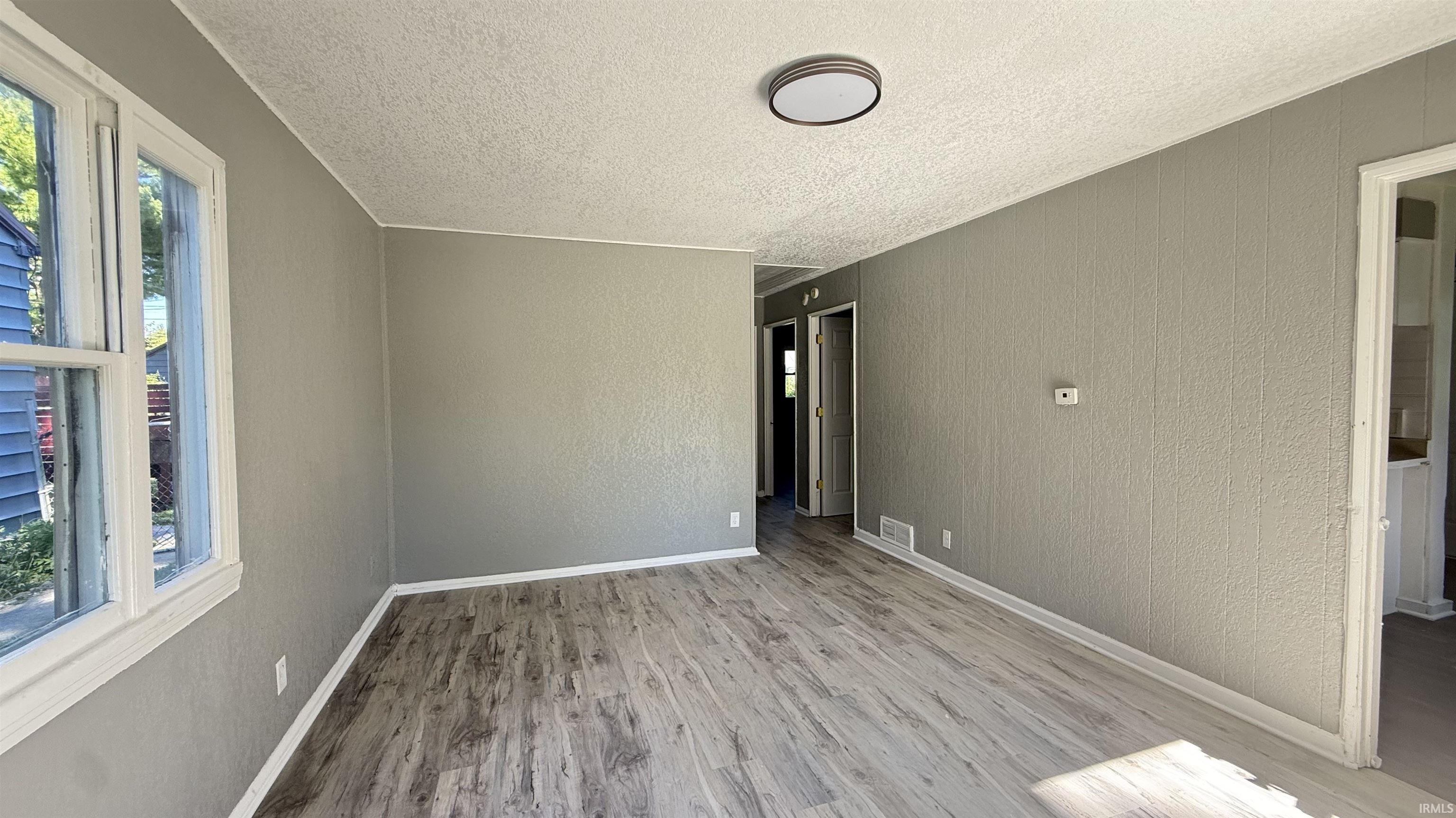 Spacious room featuring wood-finish flooring, light grey walls, and a white textured ceiling