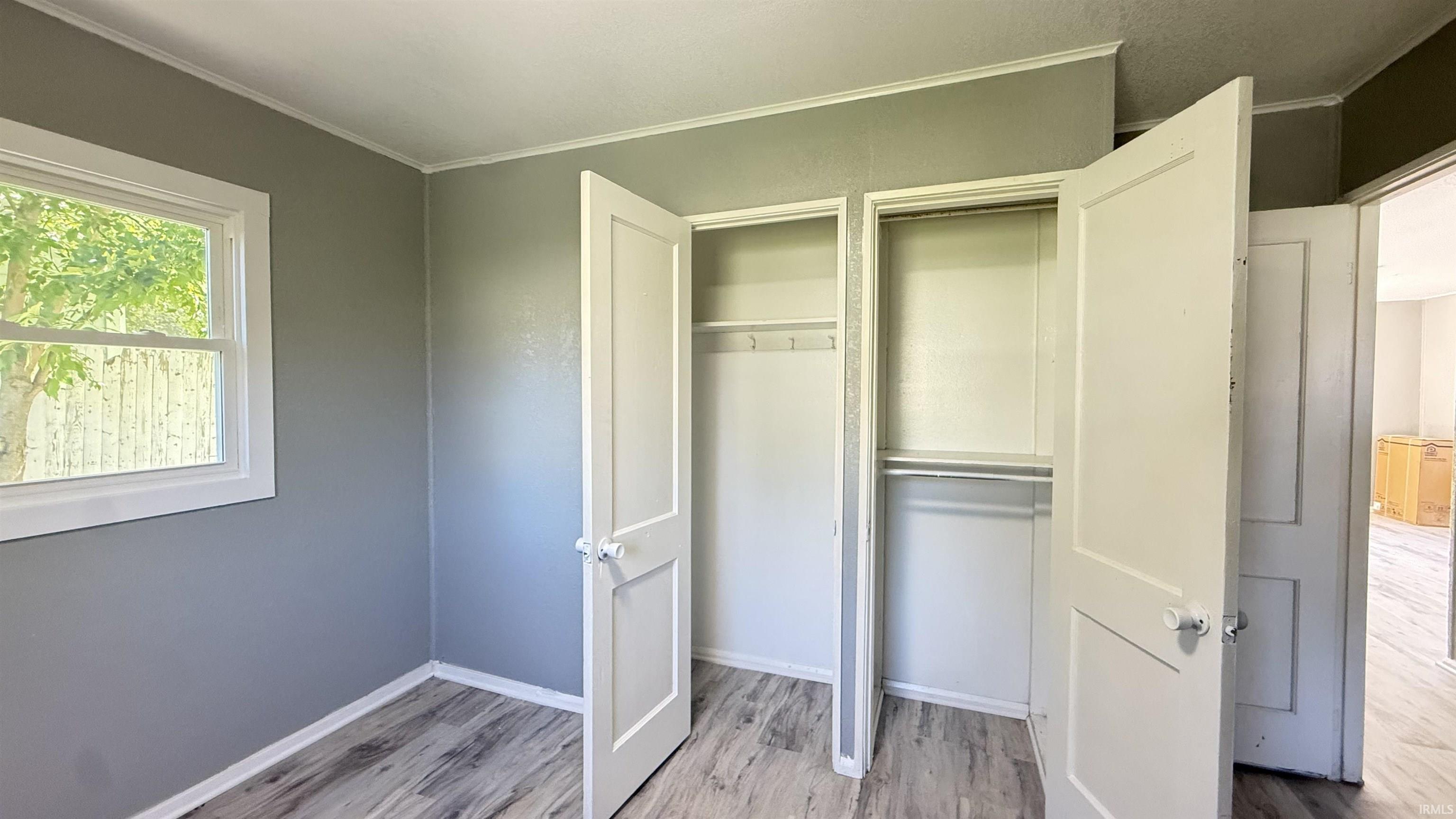 Bedroom featuring wood-finish flooring, a white-framed window, and a double-door closet with interior hanging rods and shelving