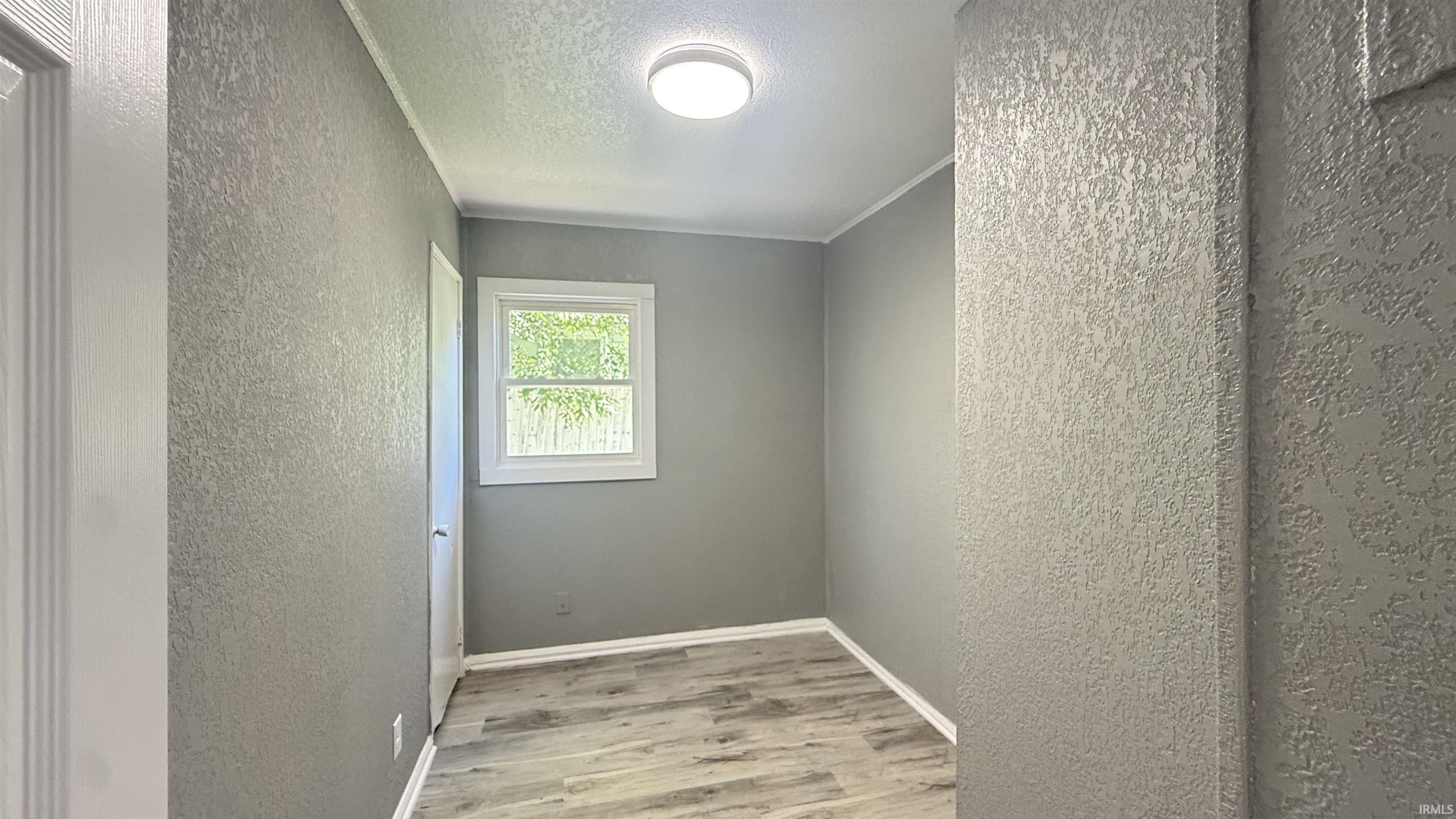 Room featuring wood-finish flooring, textured gray walls, white trim, a single window, and a flush-mount ceiling light fixture