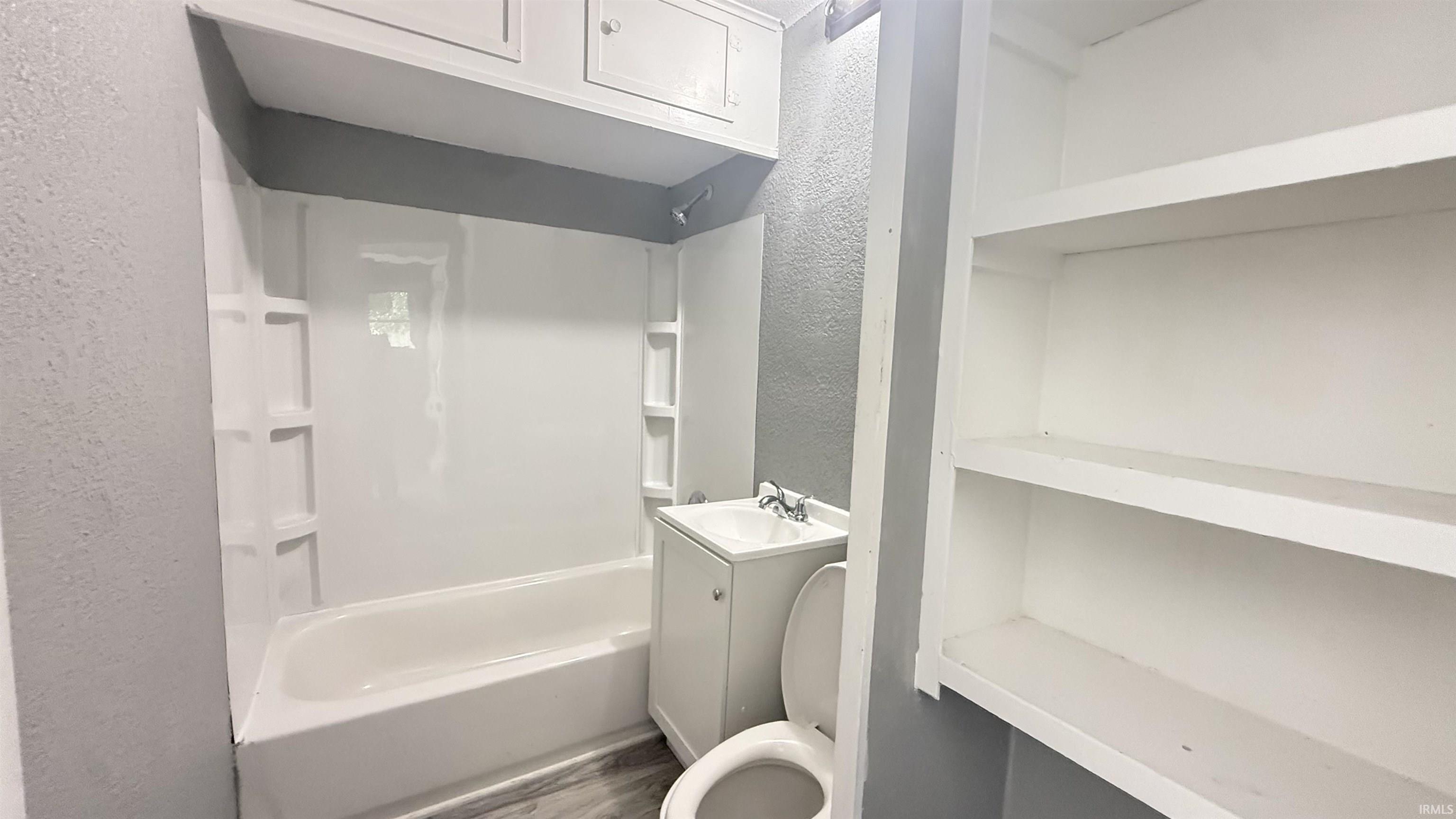 Bathroom featuring a white bathtub and shower surround, vanity with an integrated sink, built-in shelving, and overhead cabinetry