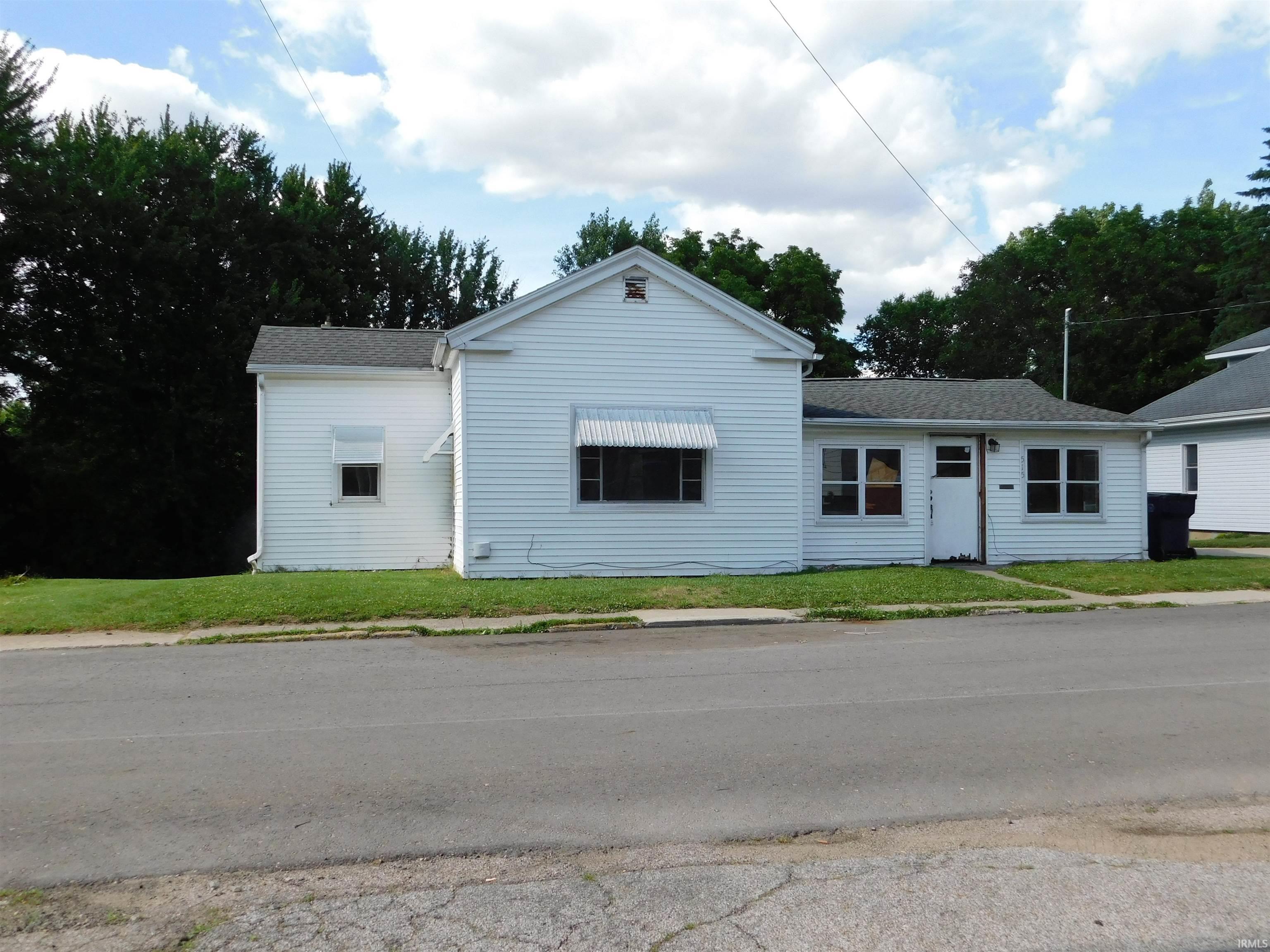 White siding exterior with multiple window awnings, a gabled roof section, and a single entry door