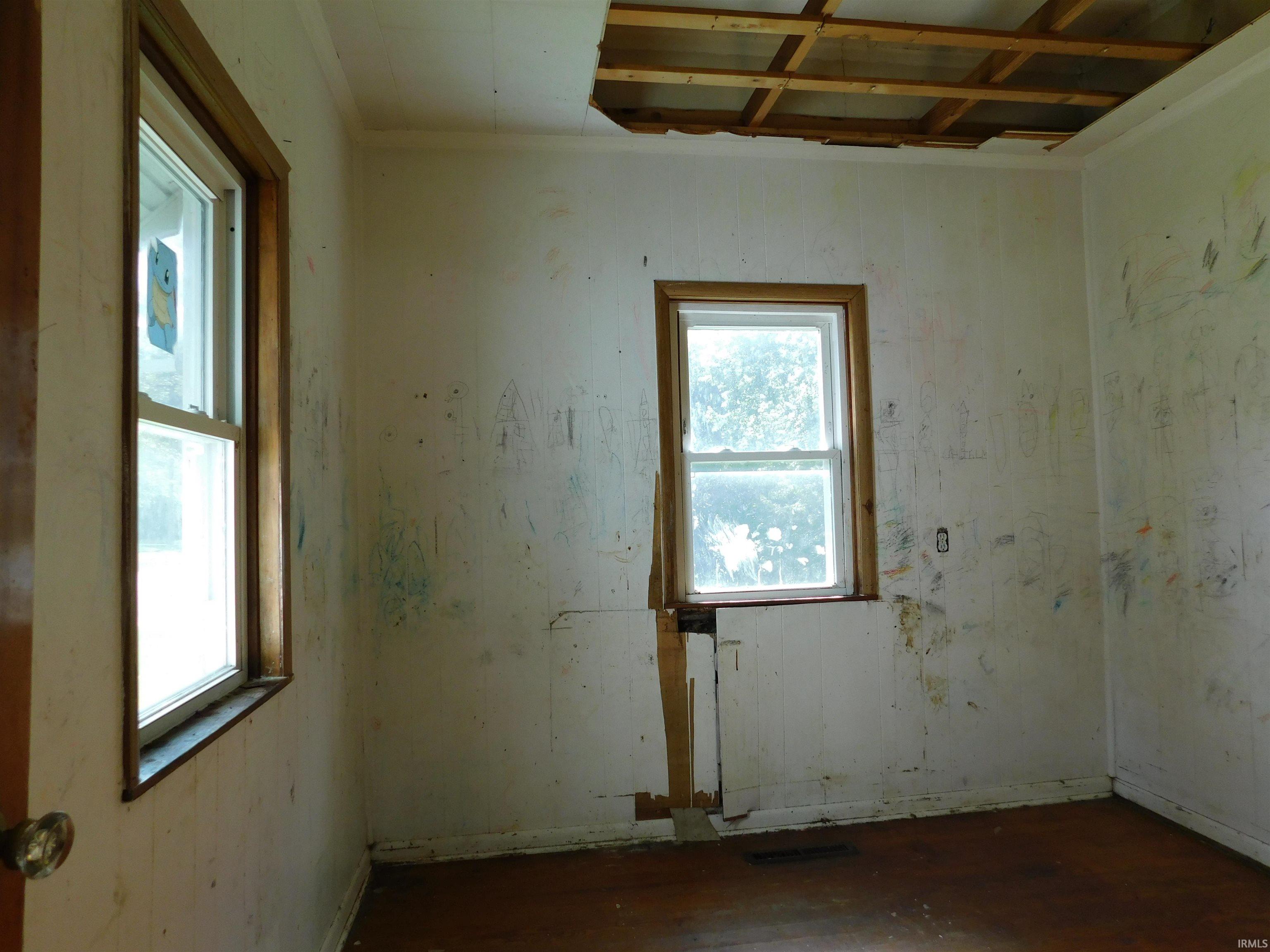 Interior space featuring wood-finish flooring, two windows with wood trim, and visible ceiling joists