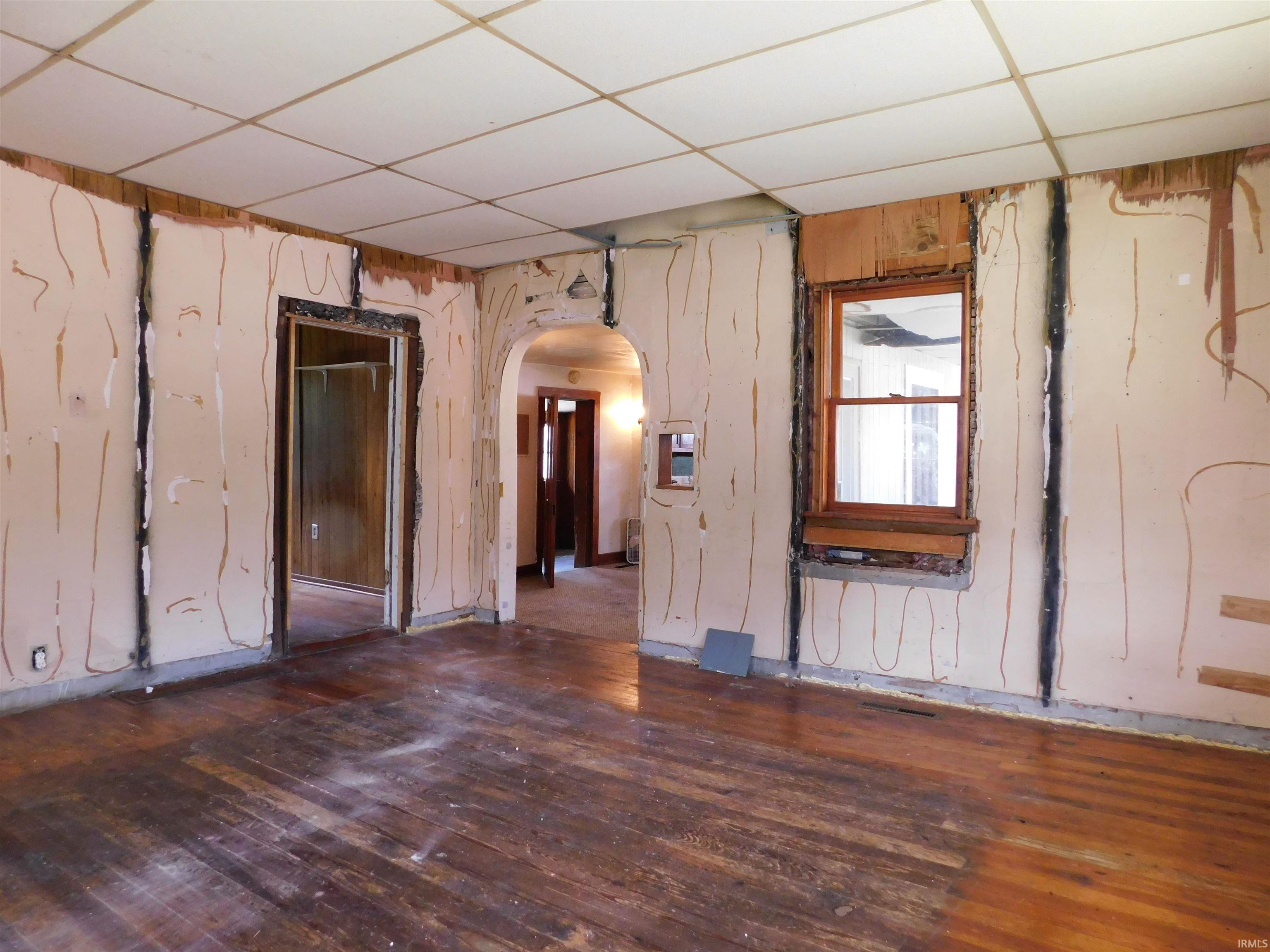 Exposed wood-finish flooring with a wood window frame and an arched doorway