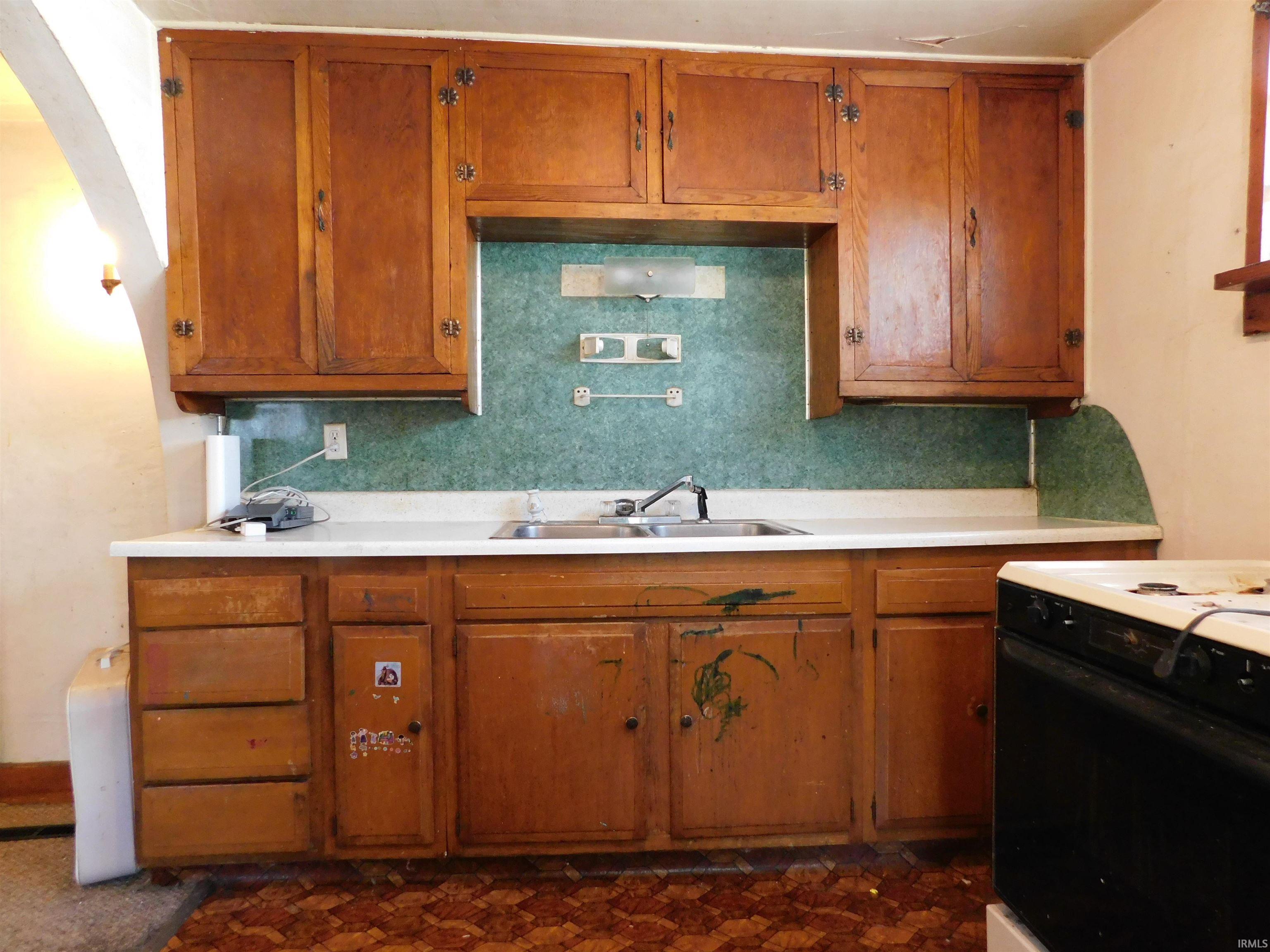 Kitchen featuring wood cabinetry, a double basin sink, white countertops, and a patterned backsplash