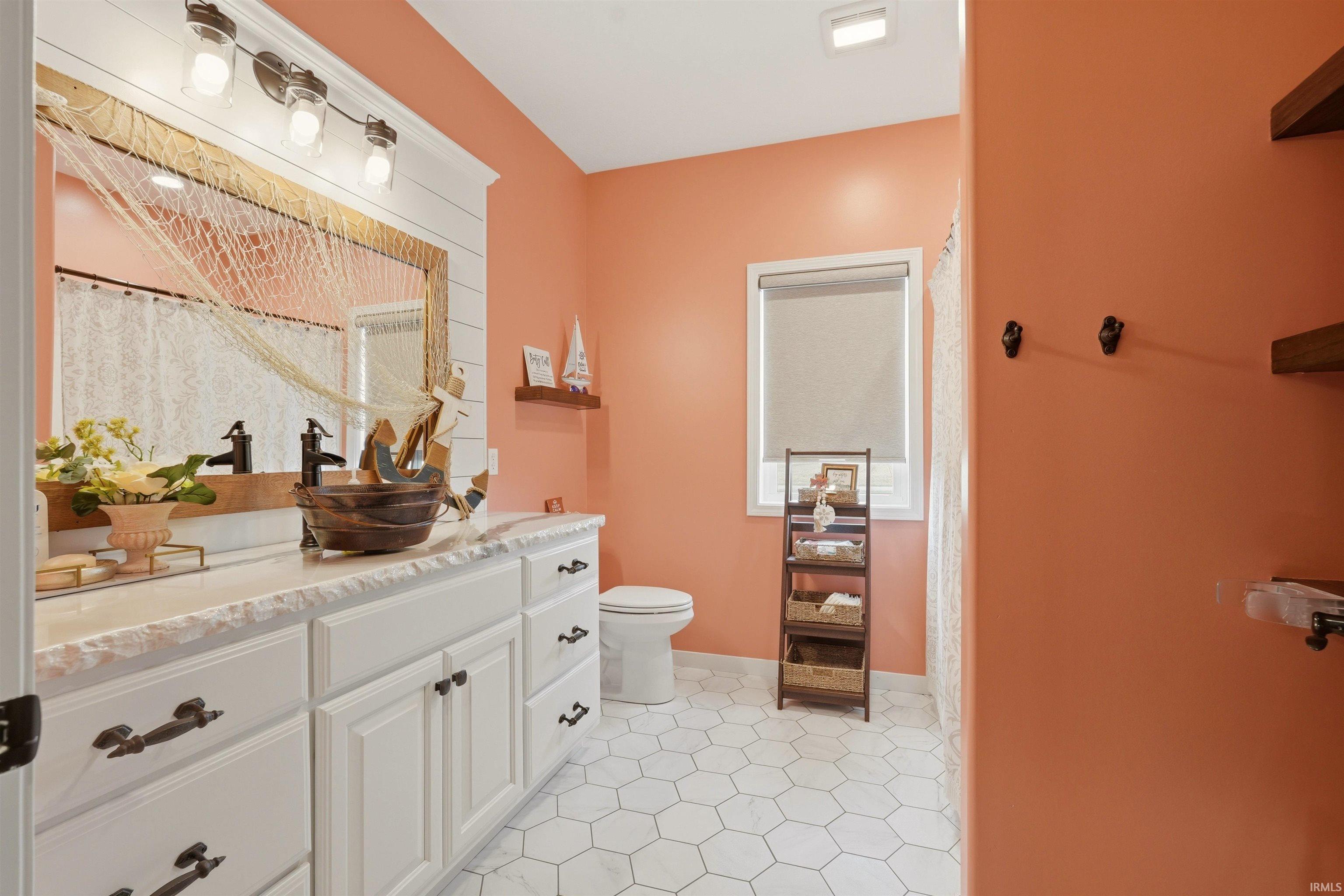 Bathroom featuring white hexagon tile flooring, a dual vanity with white cabinetry, and a framed mirror with integrated sconce lighting
