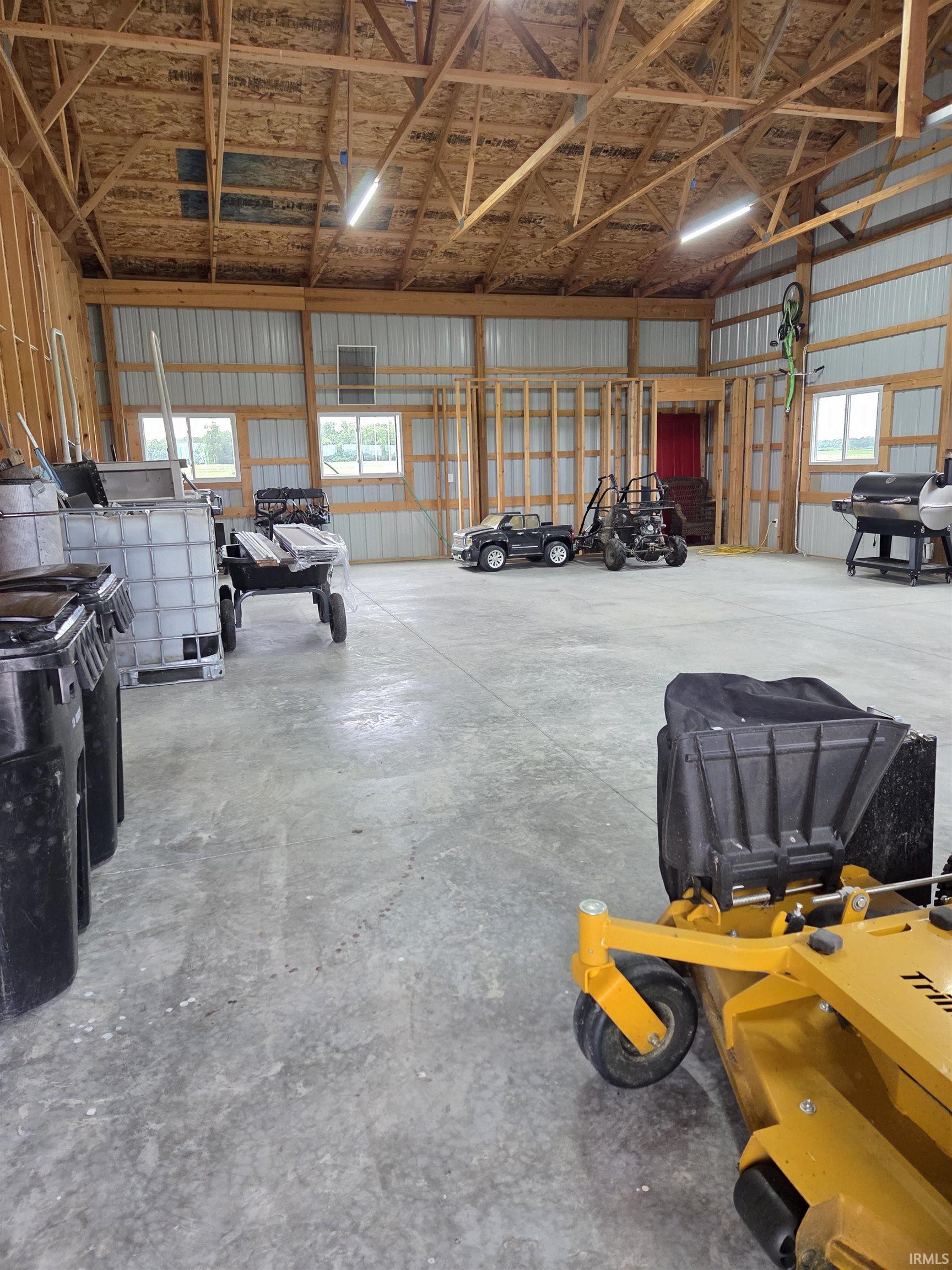 Spacious utility building featuring a concrete floor, exposed wooden truss ceiling, and multiple windows providing natural illumination