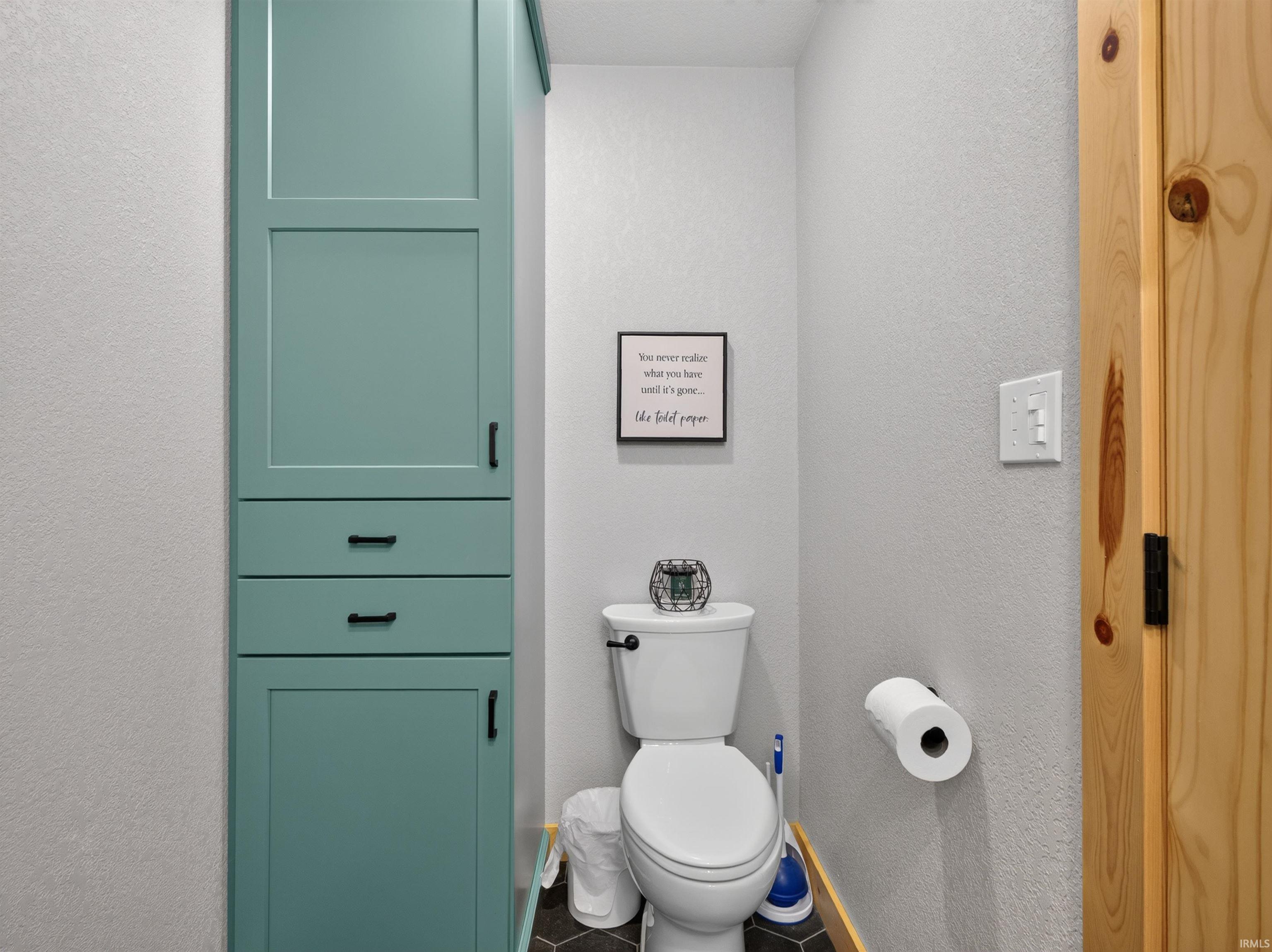 Compact powder room featuring a toilet, a teal built-in storage cabinet with two drawers and two doors, and dark hexagonal floor tiling