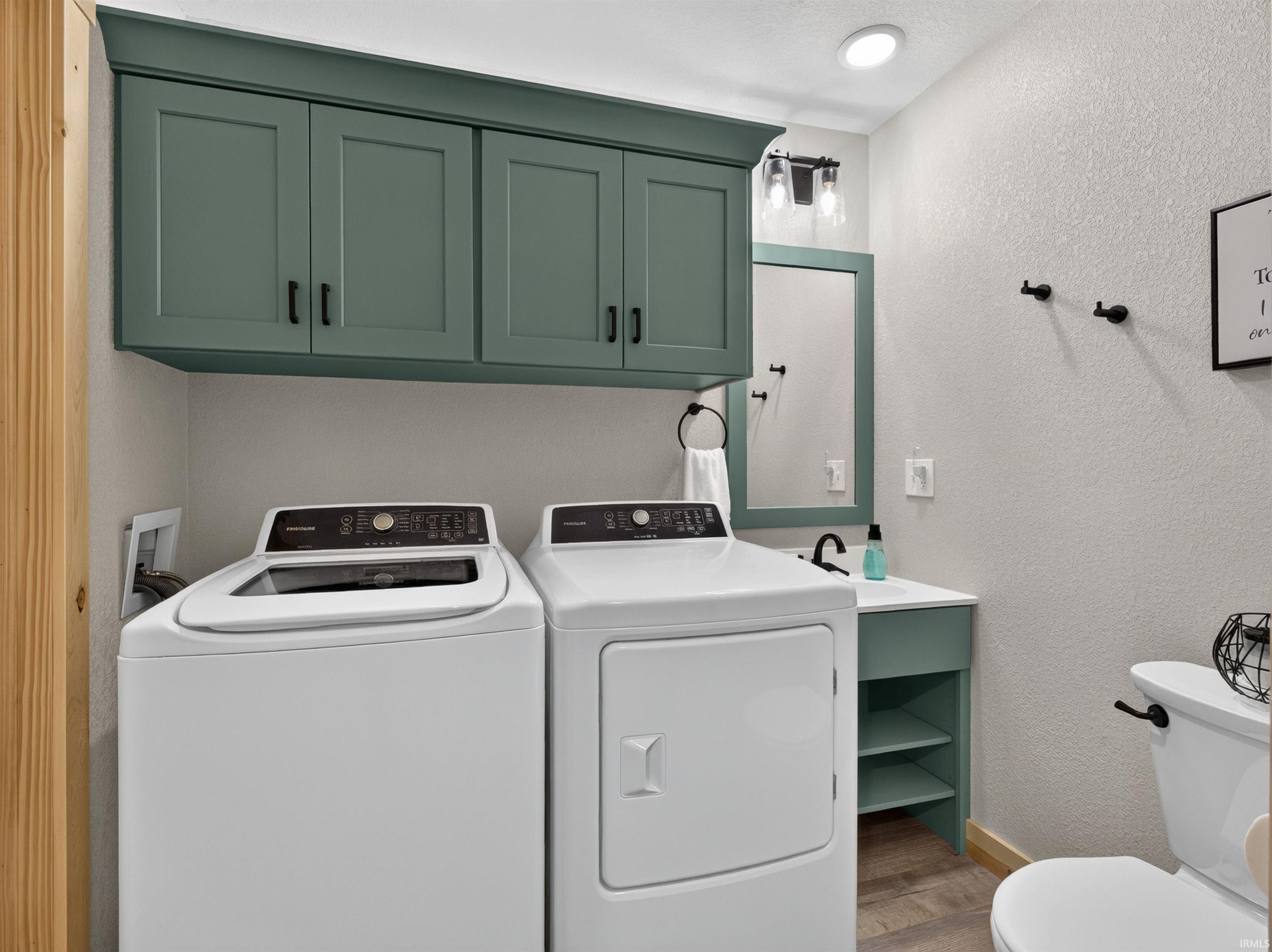 Dedicated laundry area featuring abundant overhead cabinetry in a soft green finish, complement by a coordinating vanity with open shelving