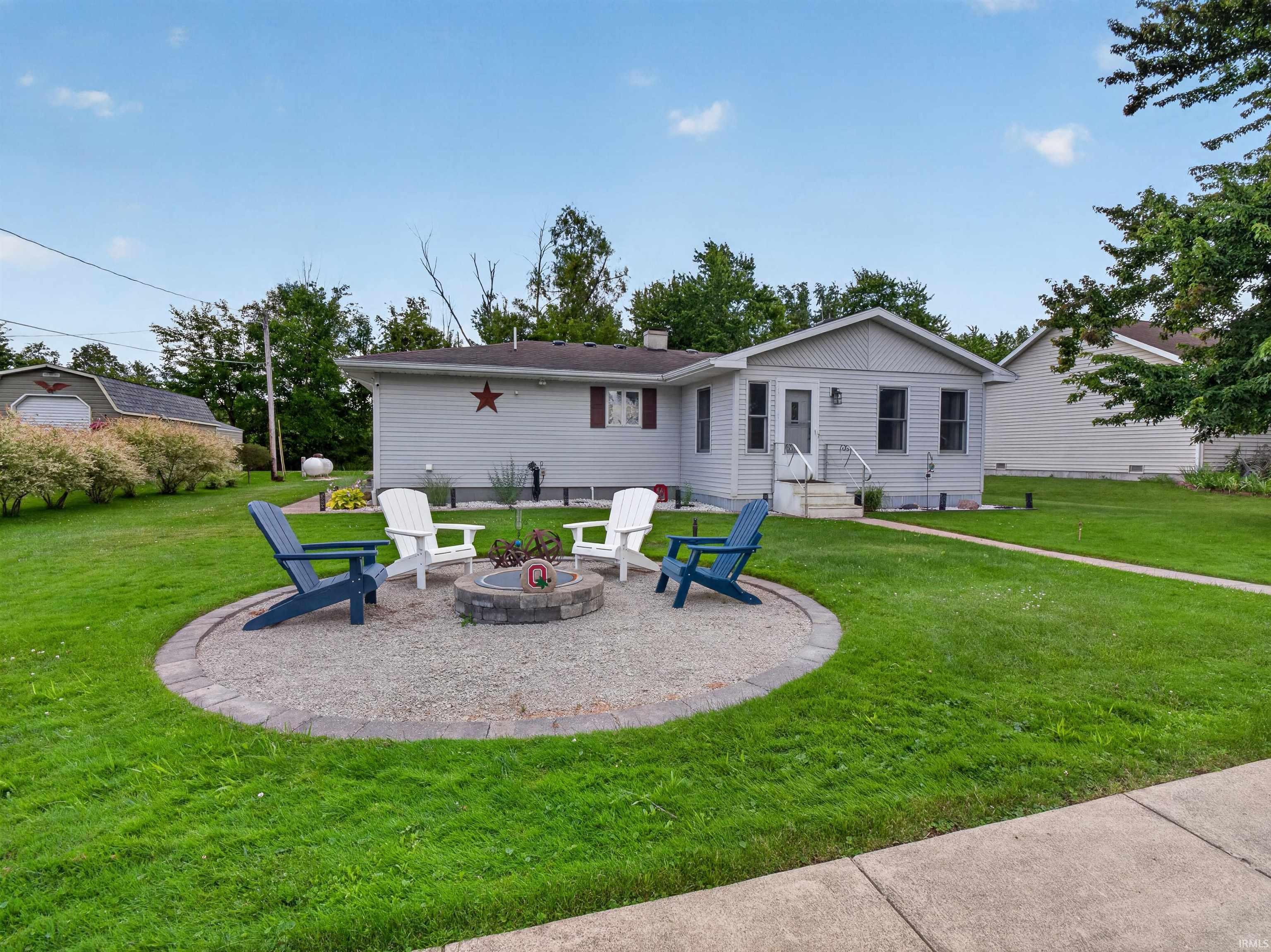 Exterior featuring light gray siding, a covered entry, and a stone fire pit area